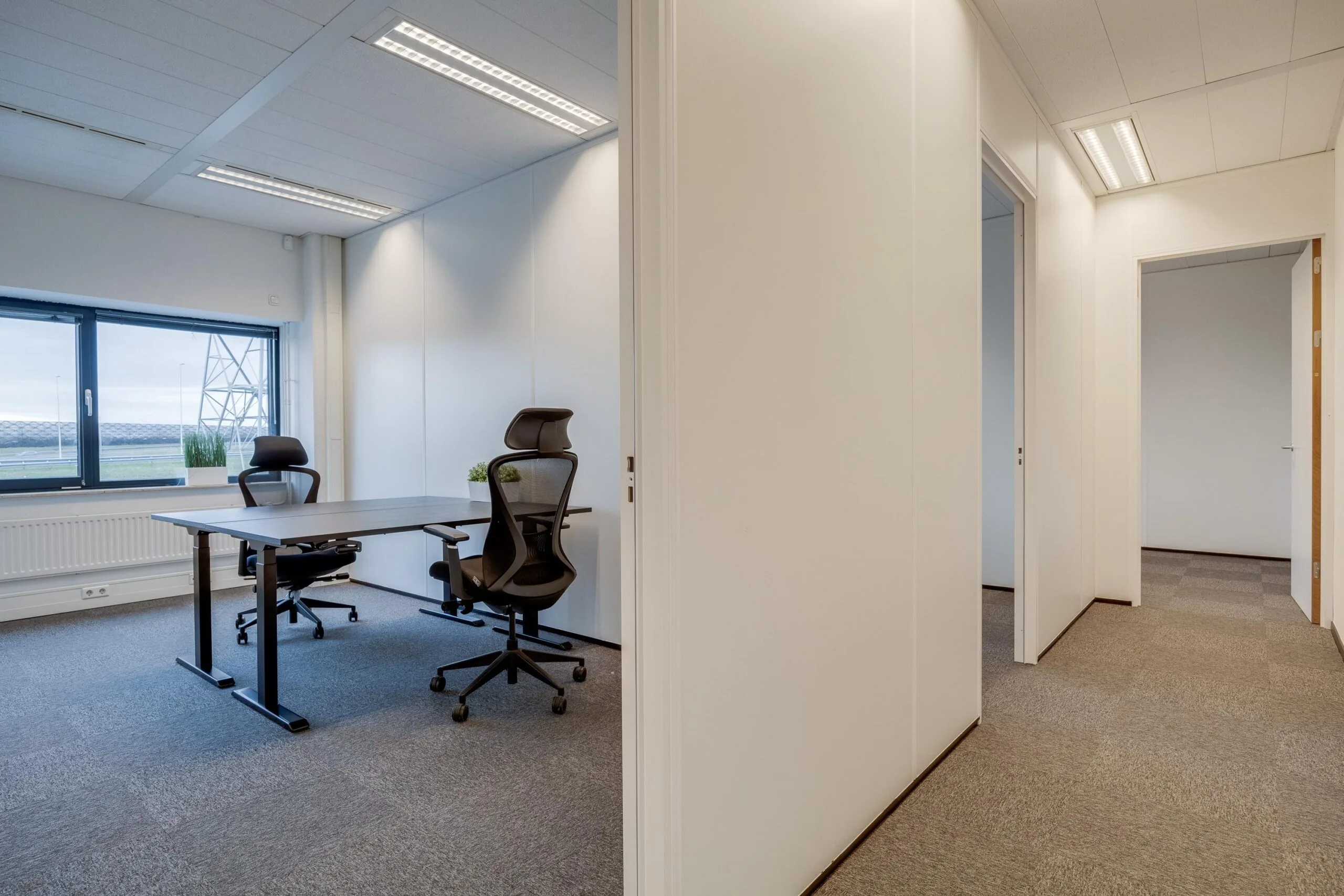Een modern kantoorinterieur met bureaus, stoelen en een groot raam met uitzicht naar buiten.