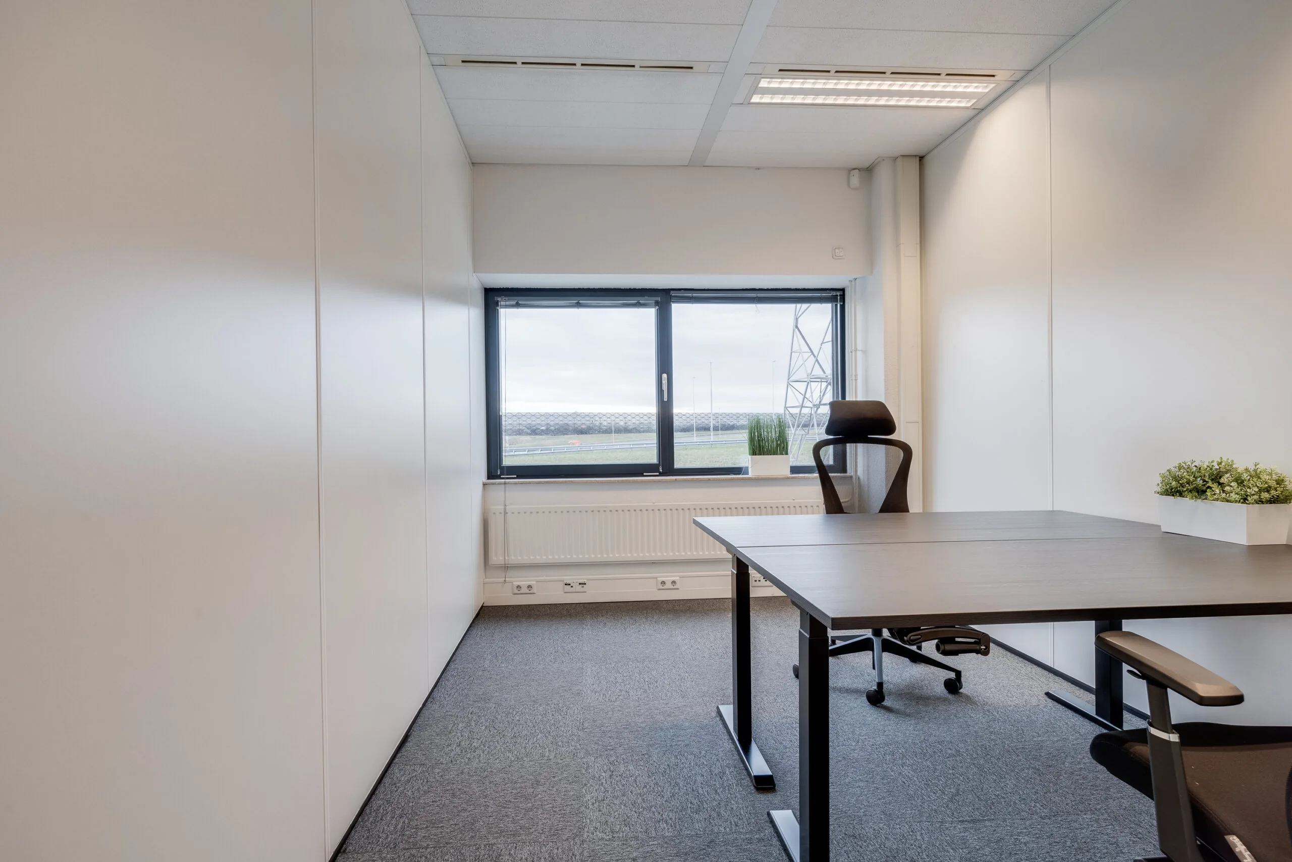 Een moderne, lege kantoorruimte met een raam en een enkel bureau met een bureaustoel.