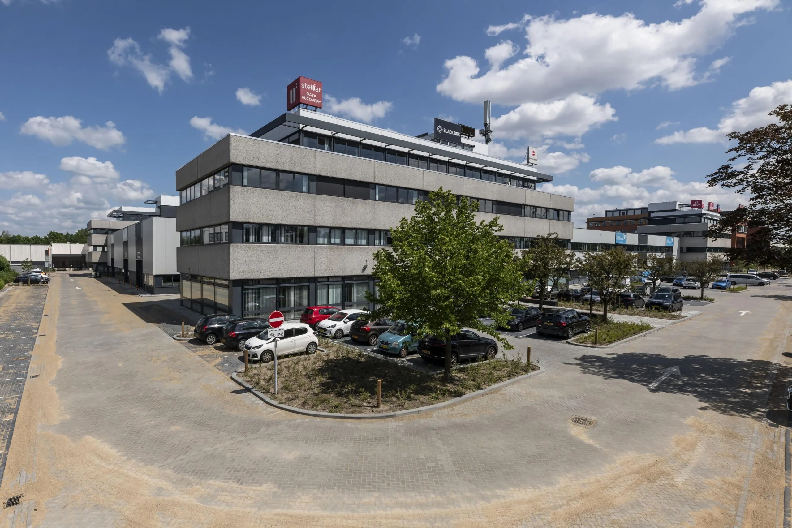 Bedrijventerrein met modern kantoorpand en parkeerplaats onder een blauwe lucht.