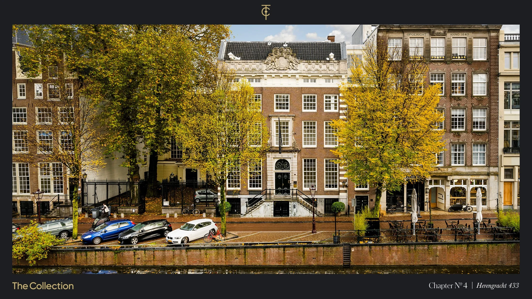Gevel van een historisch grachtenpand aan de Herengracht, met gekleurde bomen en geparkeerde auto's langs het water.