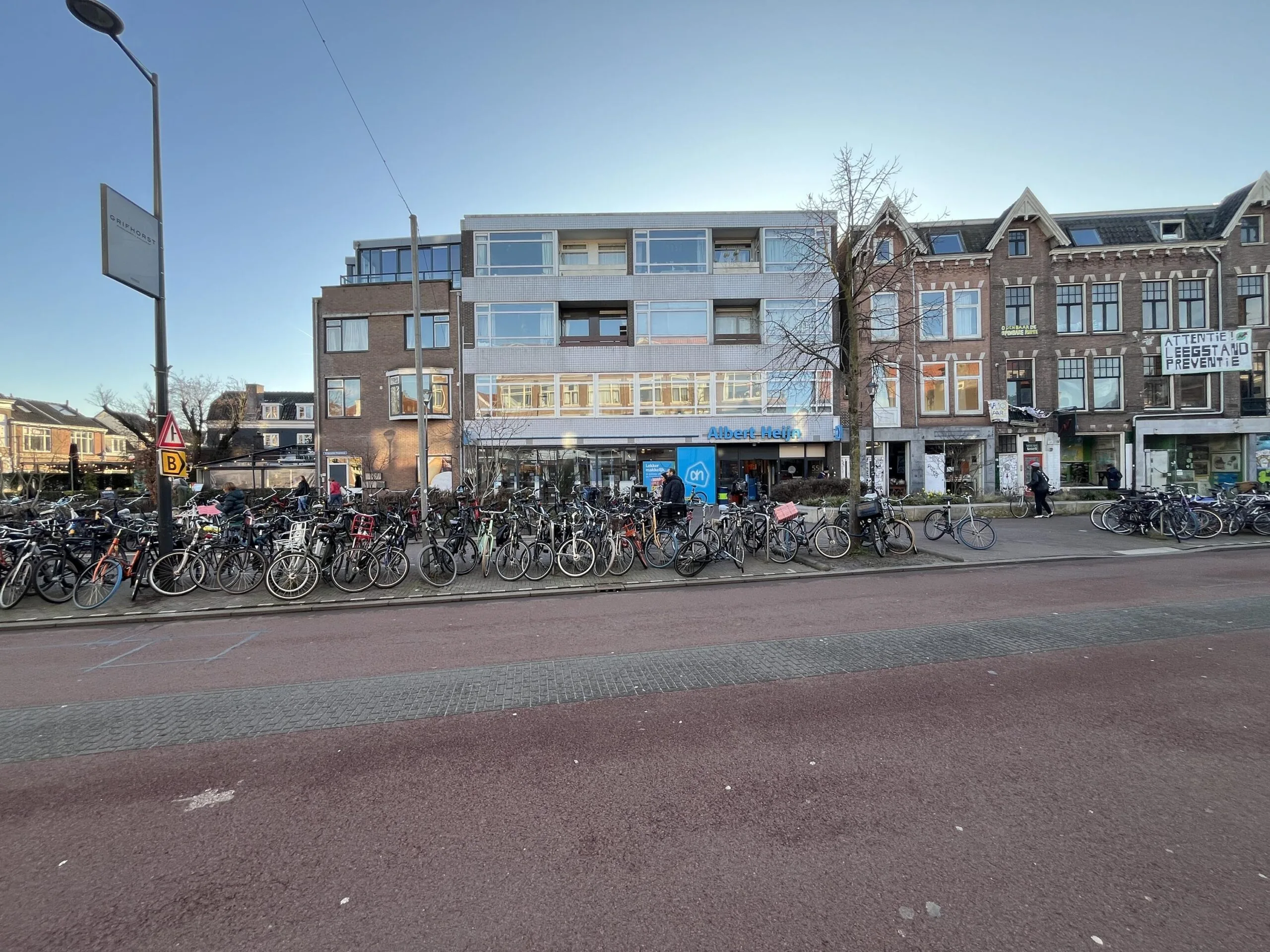 Straatbeeld van de Burgemeester Reigerstraat met geparkeerde fietsen en de gevels van een Albert Heijn supermarkt en omliggende gebouwen.