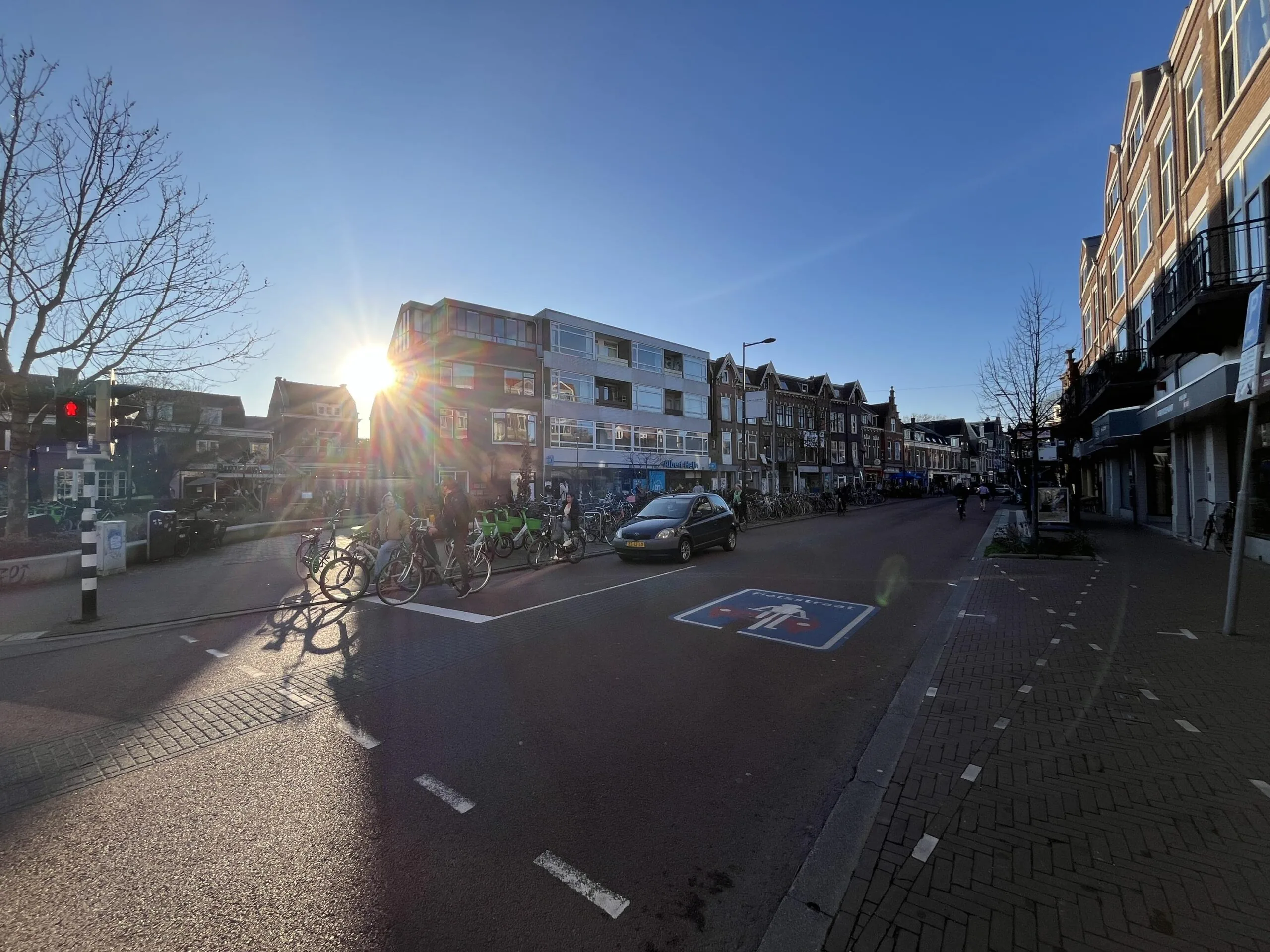 Een straat vol met fietsen en een auto in het zonlicht op de Burgemeester Reigerstraat.