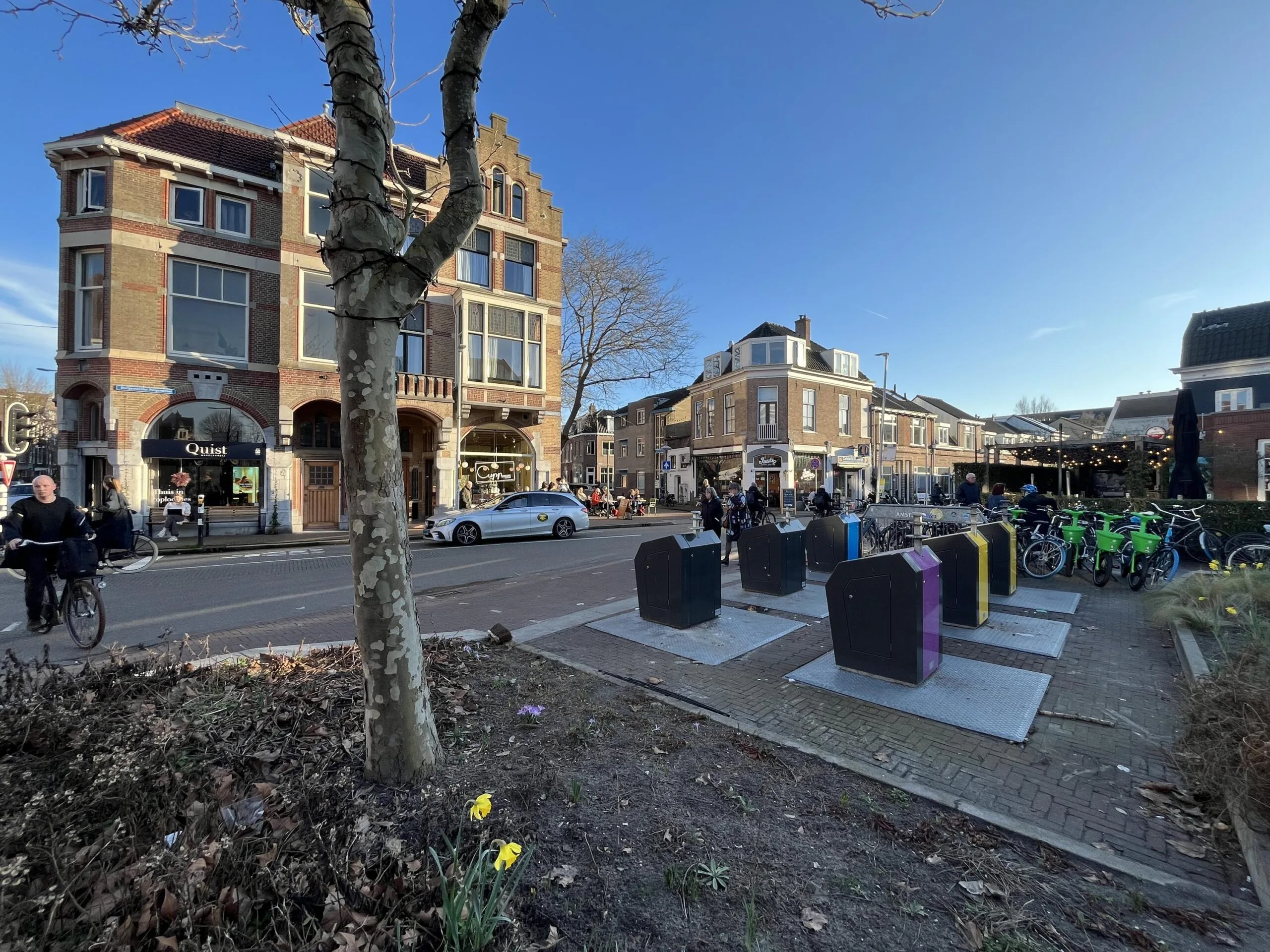 Straatbeeld van de Burgemeester Reigerstraat met een historisch gebouw, fietsenstalling en passerende voetgangers.