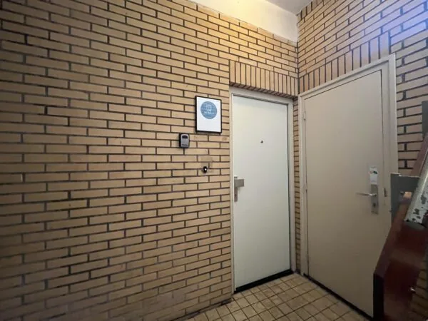 Een hoek van een gang met twee witte deuren en een betegelde vloer, omringd door bakstenen muren.