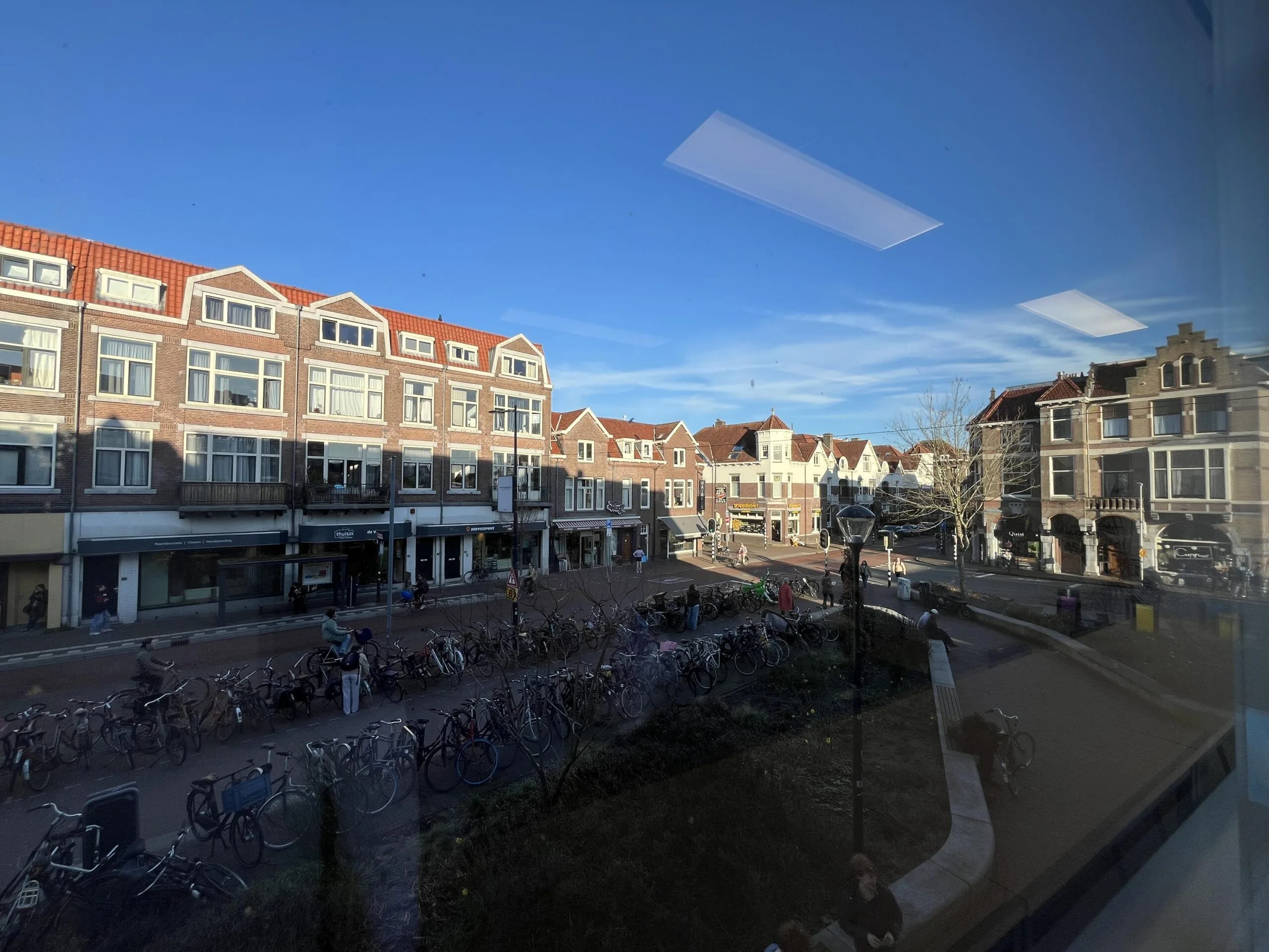 Straatbeeld van de Burgemeester Reigerstraat met fietsenrekken en historische gebouwen onder een blauwe lucht.