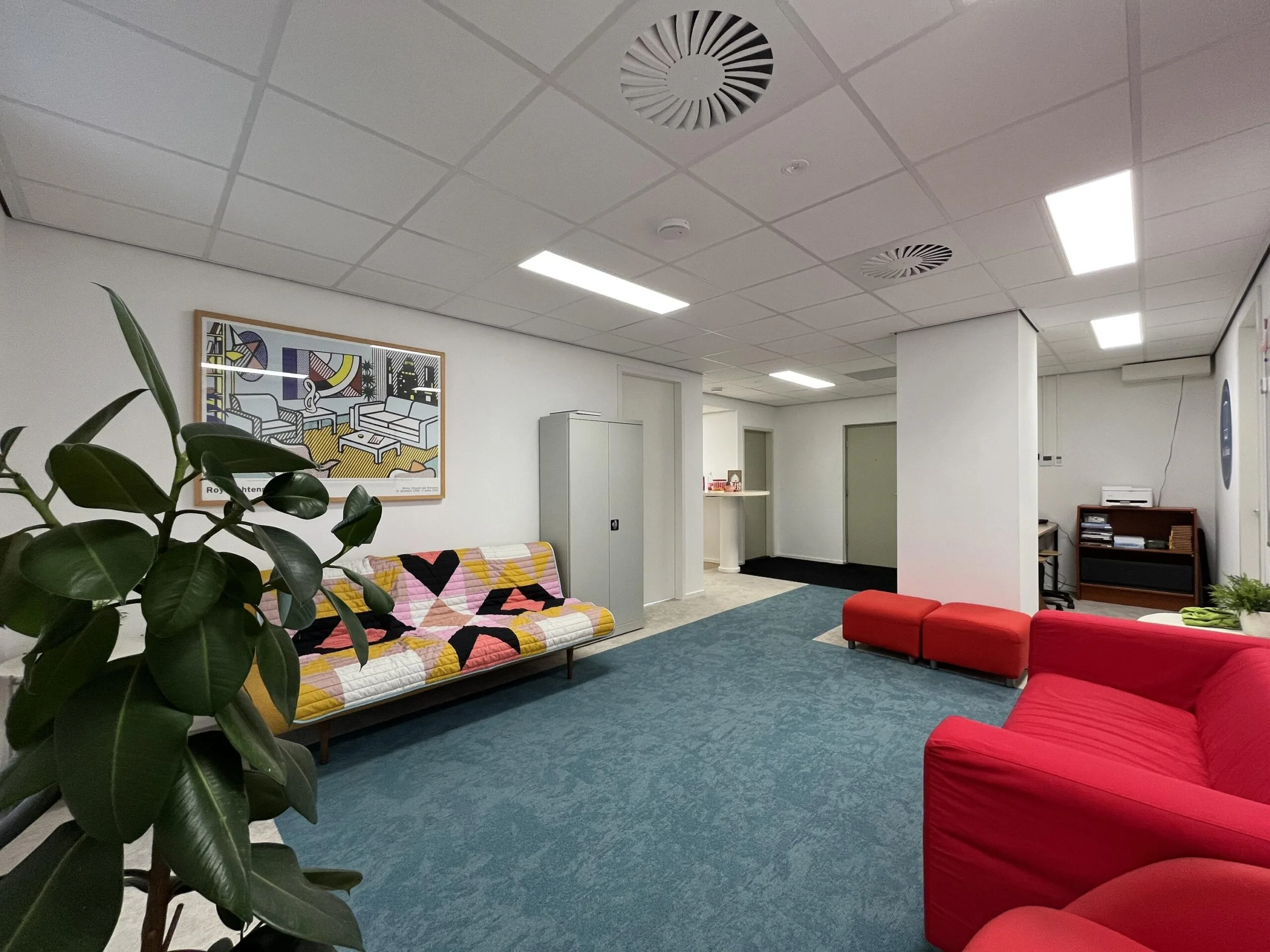 Een moderne wachtkamer met kleurrijke meubels en een grote plant.