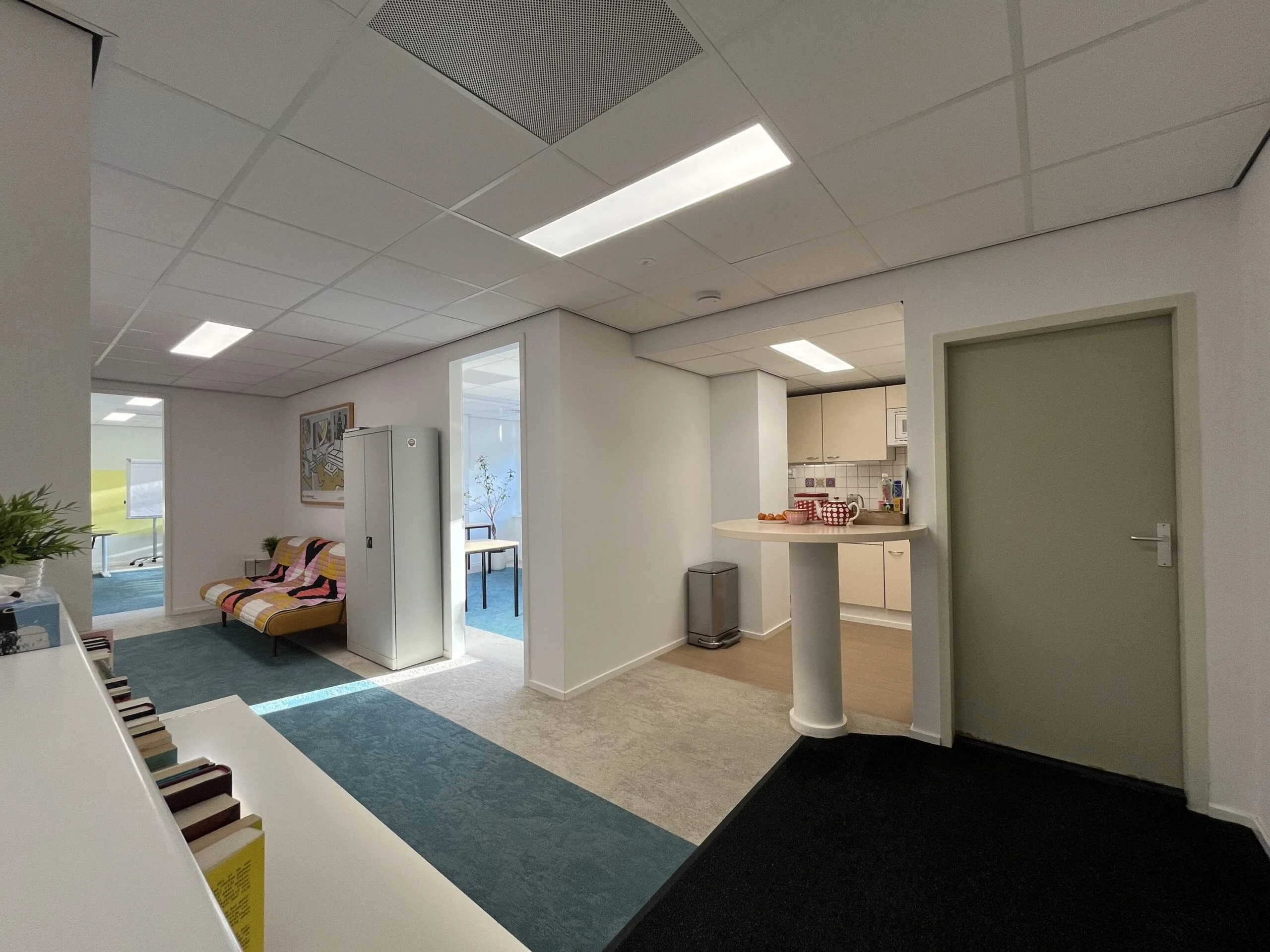 Een modern ingerichte wachtkamer met een bank, keukentje en boekenkast.