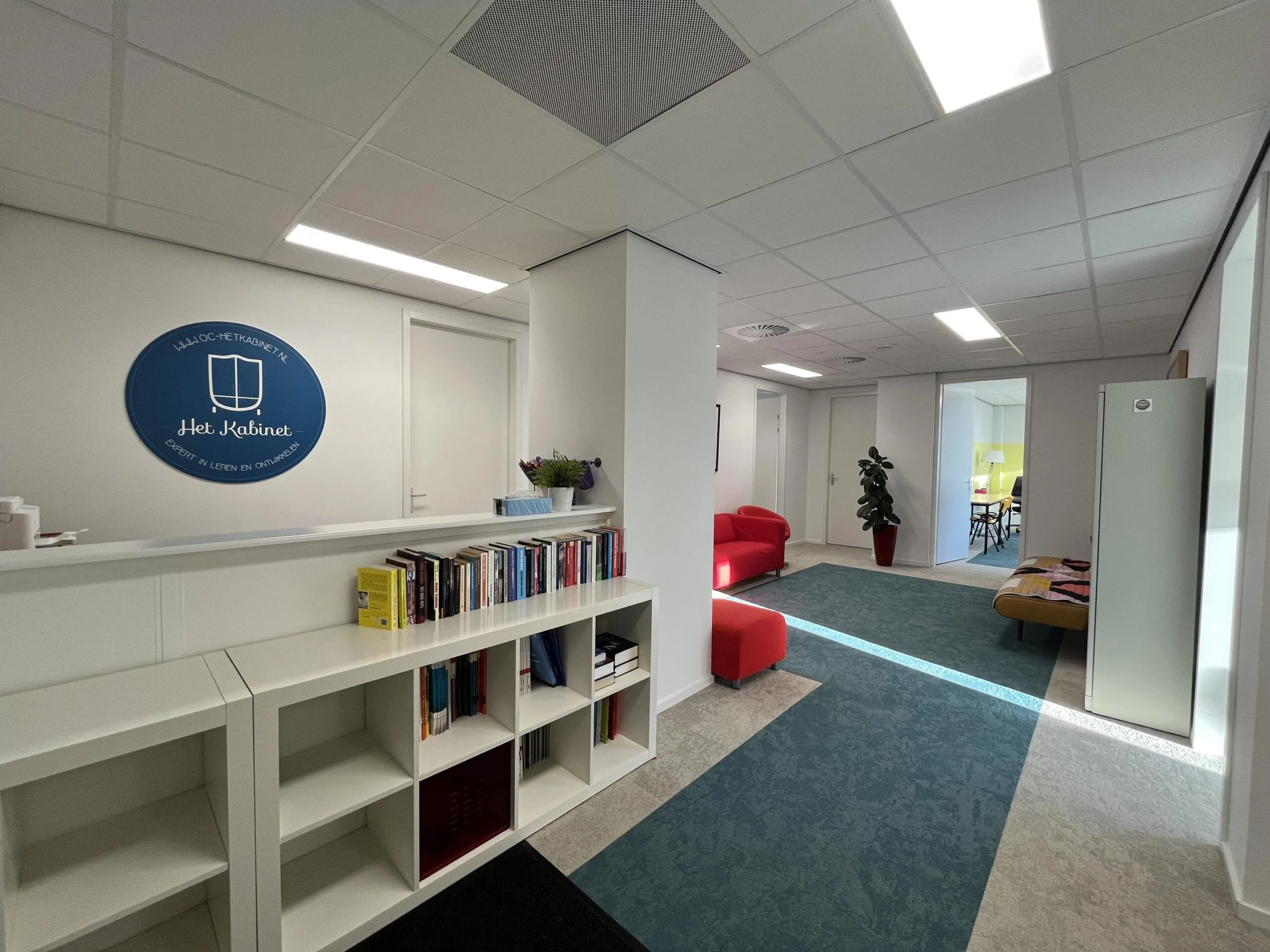 Een lichte en moderne kantoorruimte met een boekenkast en het logo van "Het Kabinet" aan de muur.