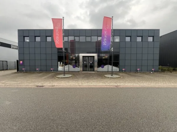 Een modern kantoorgebouw met twee vlaggen bij de hoofdingang op een bewolkte dag.