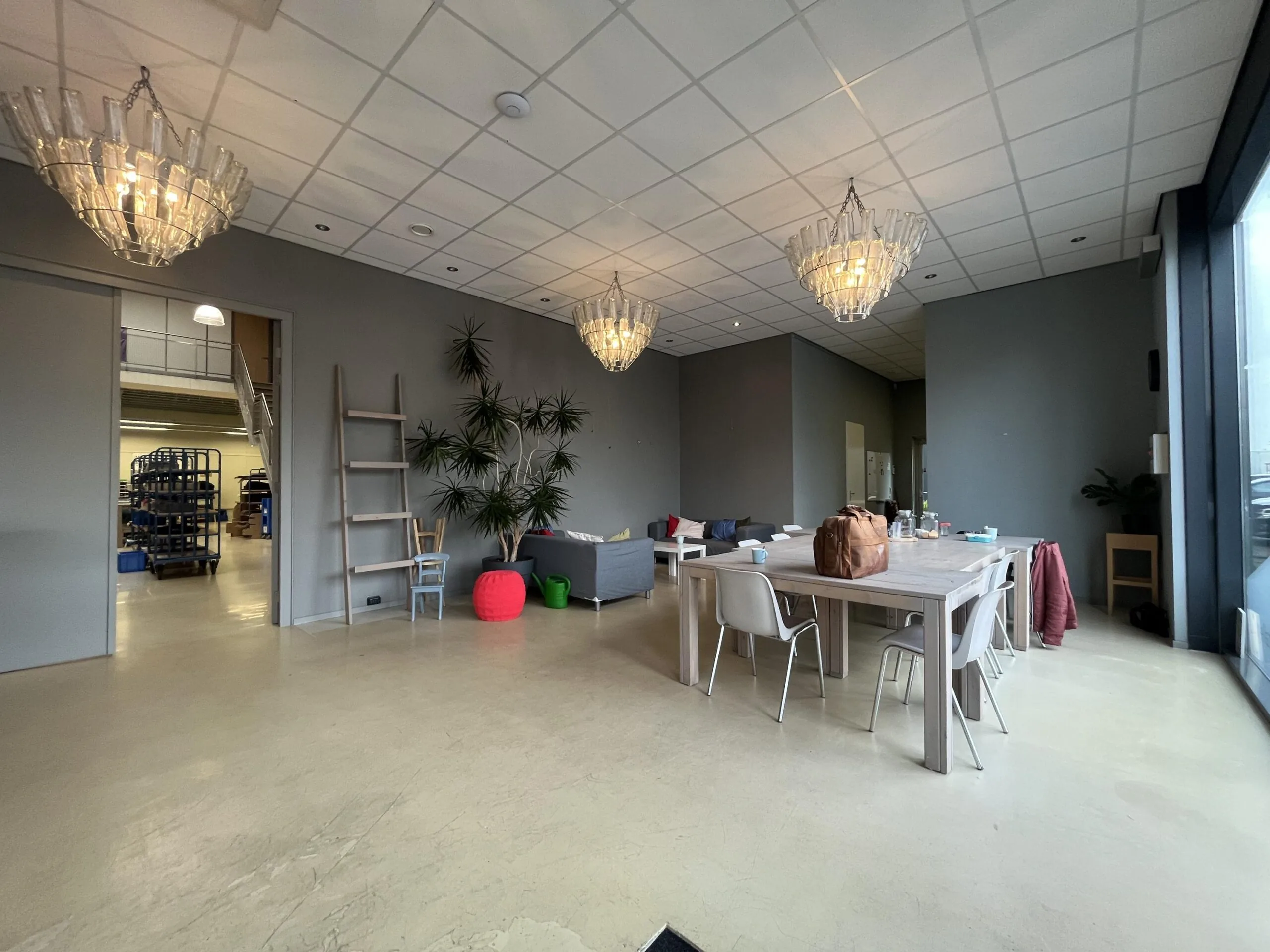 Een moderne ruimte met een houten tafel en stoelen, omgeven door planten en hangende lampen.