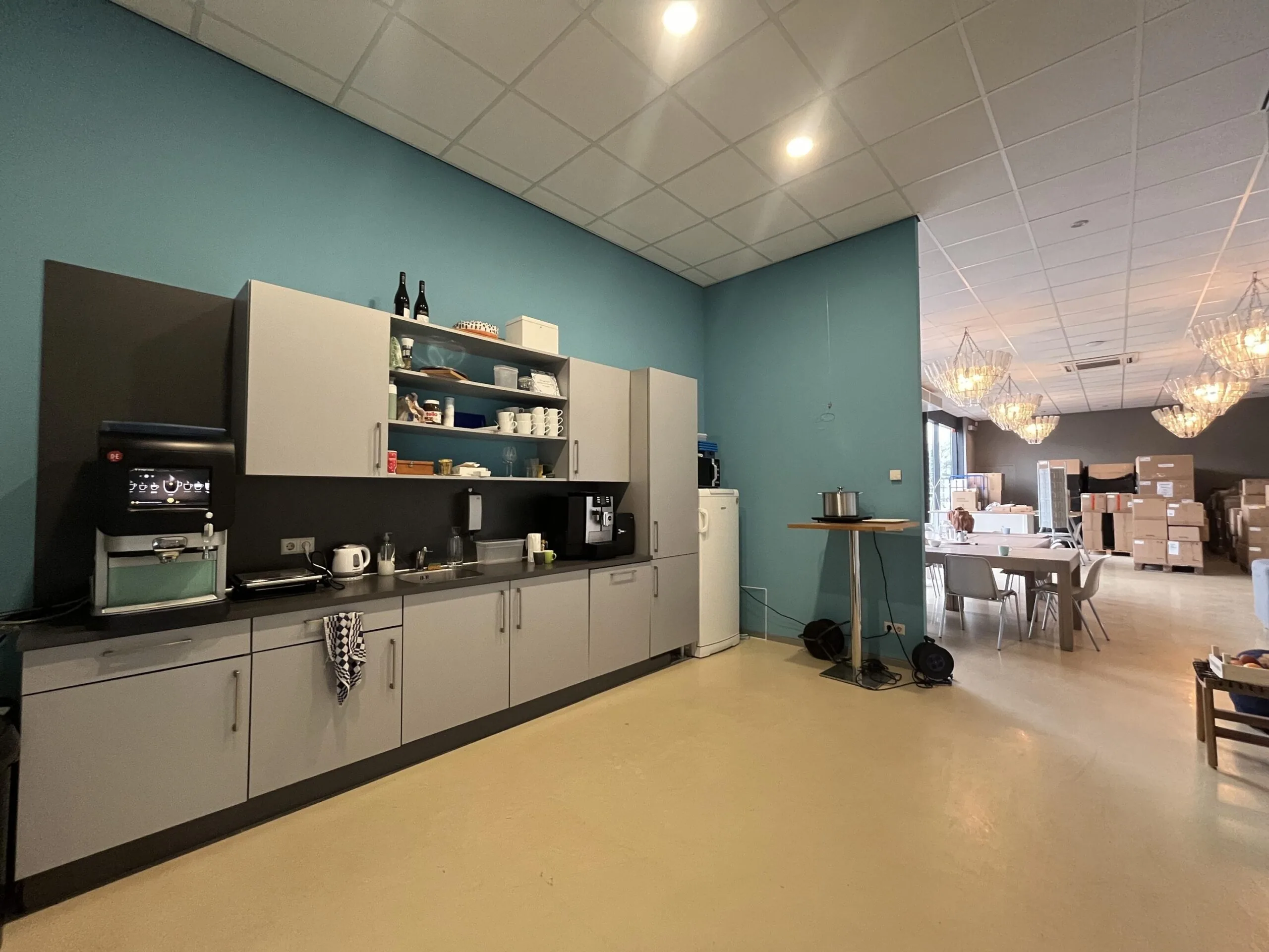 Een modern ingerichte keukenruimte met kasten, een koffiezetapparaat en een tafel in een lichte omgeving.
