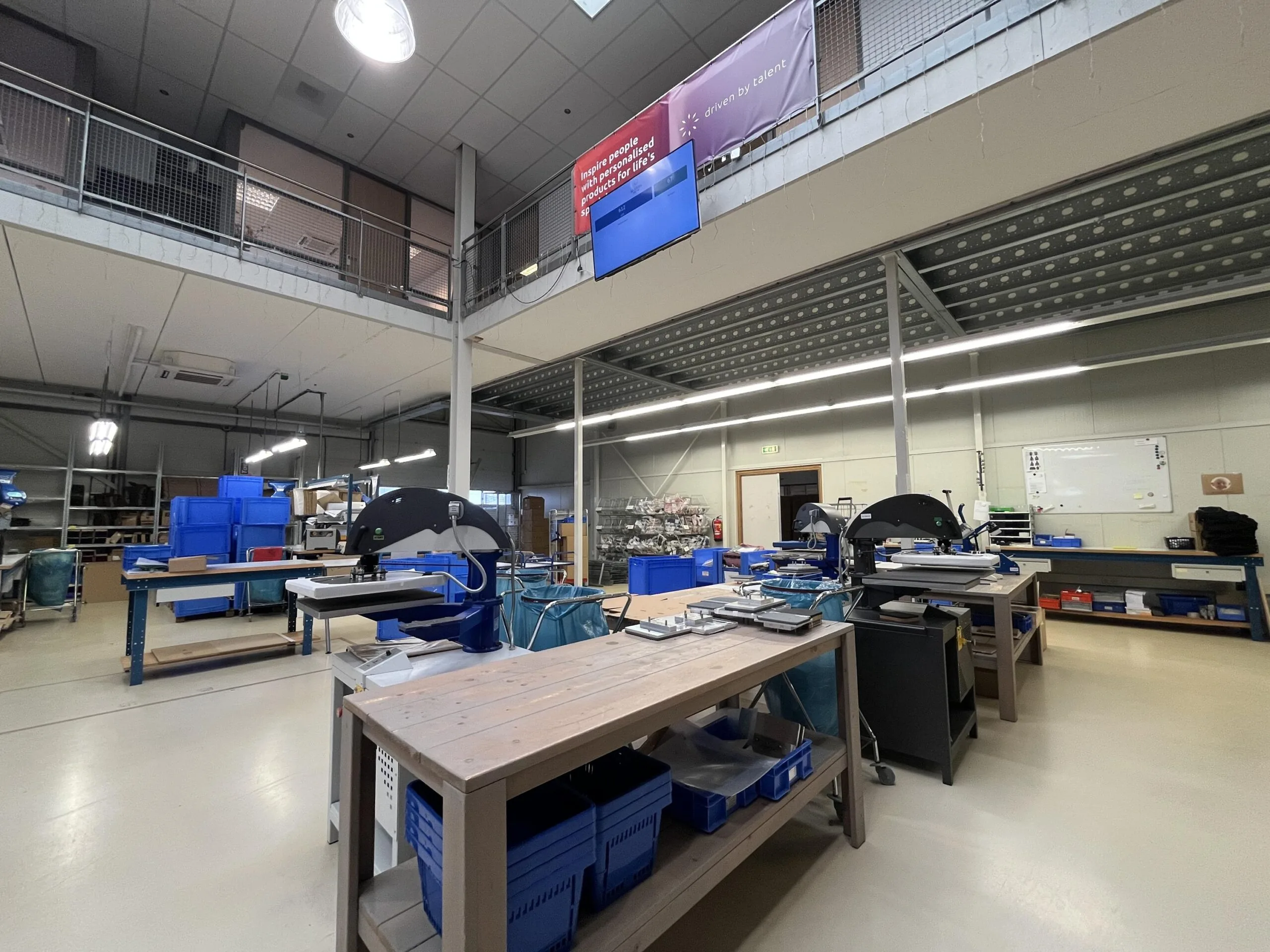 Interieur van een moderne werkplaats met tafels, machines en blauwe bakken.