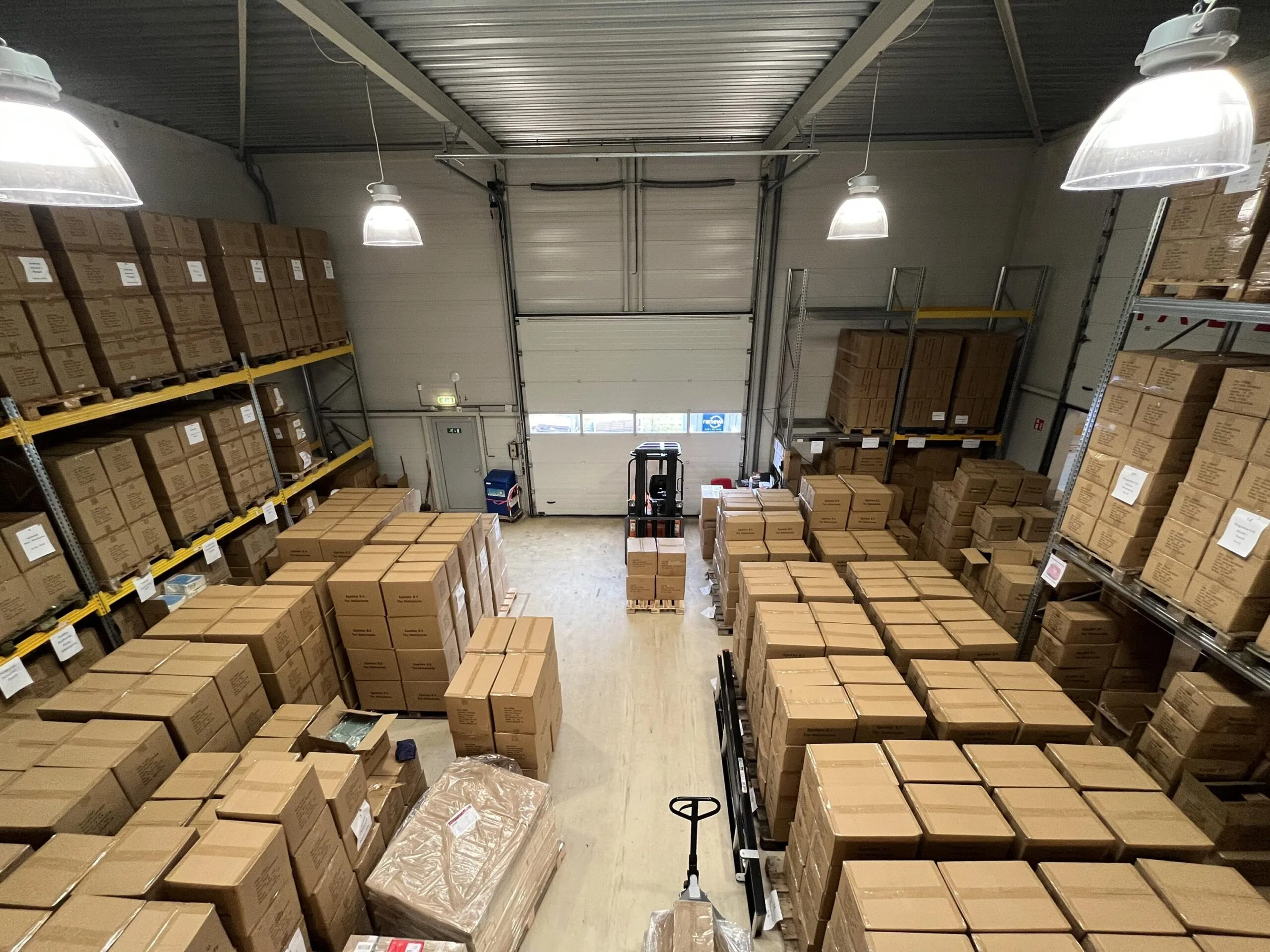 Opslagruimte gevuld met gestapelde kartonnen dozen en een vorkheftruck in het midden.