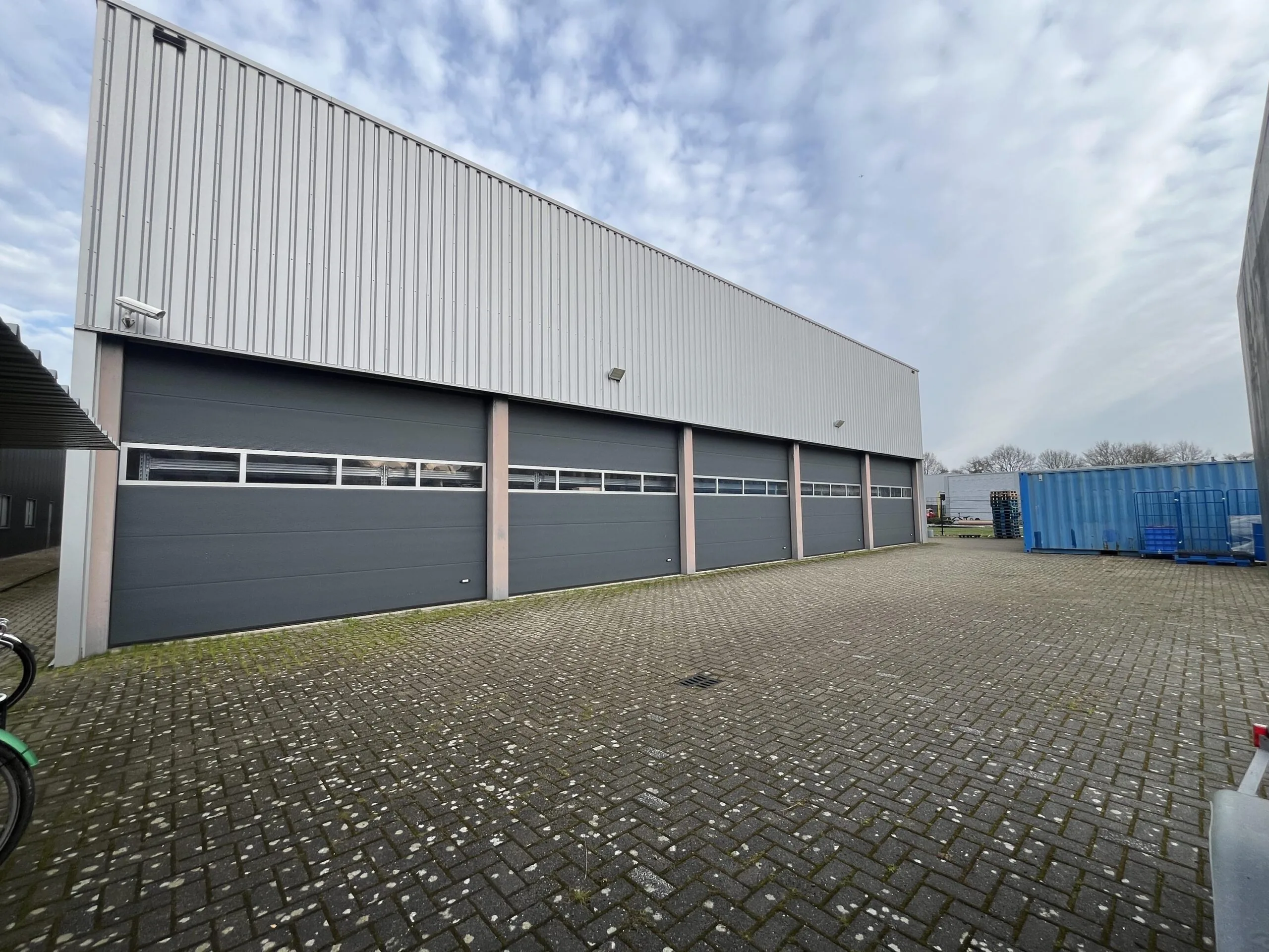 Een industrieel gebouw met meerdere garagedeuren en een betegelde parkeerplaats.