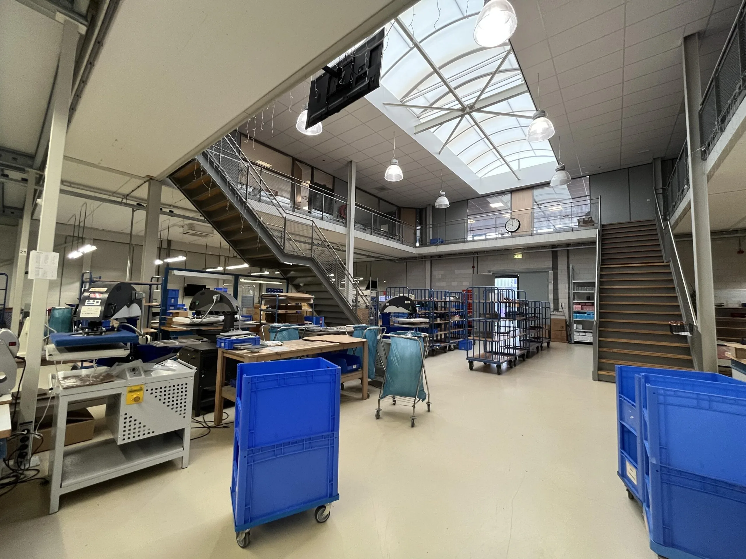 Een lichte werkplaats met machines, tafels en blauwe opslagkratten onder een grote dakkoepel.