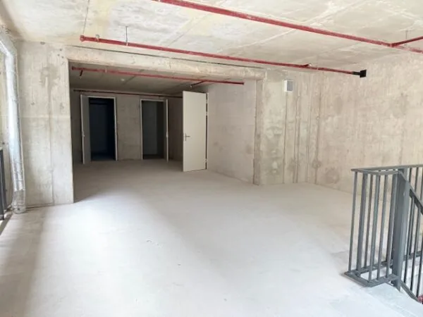 Lege betonnen ruimte met enkele geopende deuren en rode buizen aan het plafond.