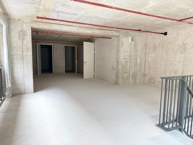 Lege betonnen ruimte met enkele geopende deuren en rode buizen aan het plafond.