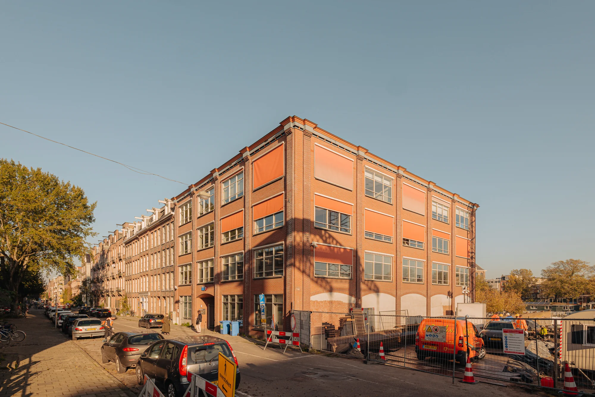 Bakstenen gebouw aan de Hoogte Kadijk met geparkeerde auto's en bouwactiviteiten op de voorgrond.