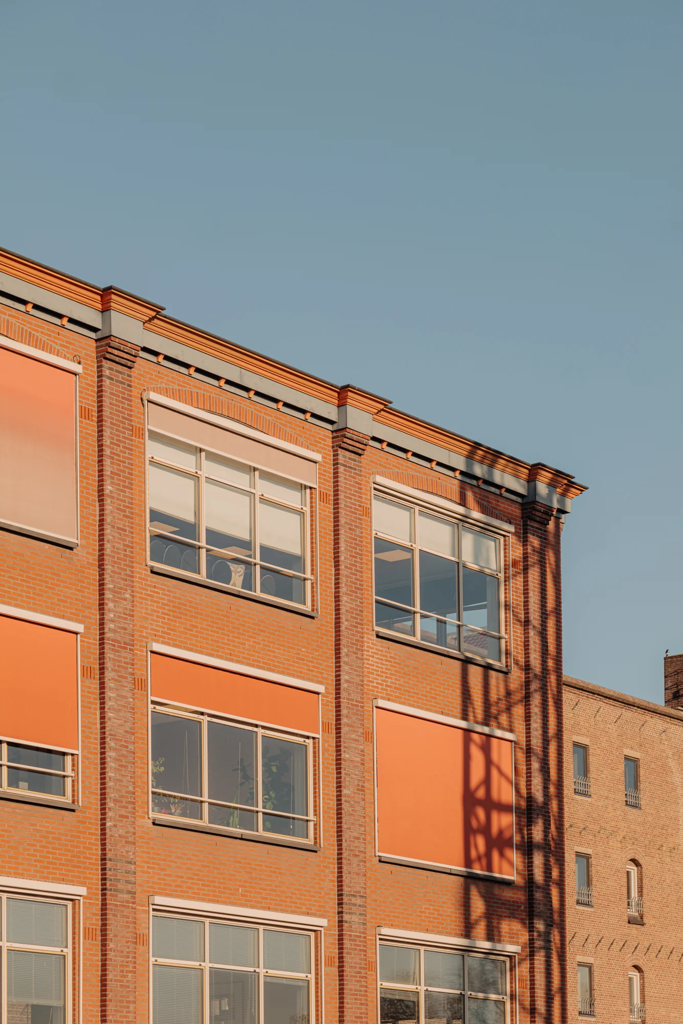 Buitenaanzicht van een bakstenen gebouw met oranje zonwering op de Hoogte Kadijk.