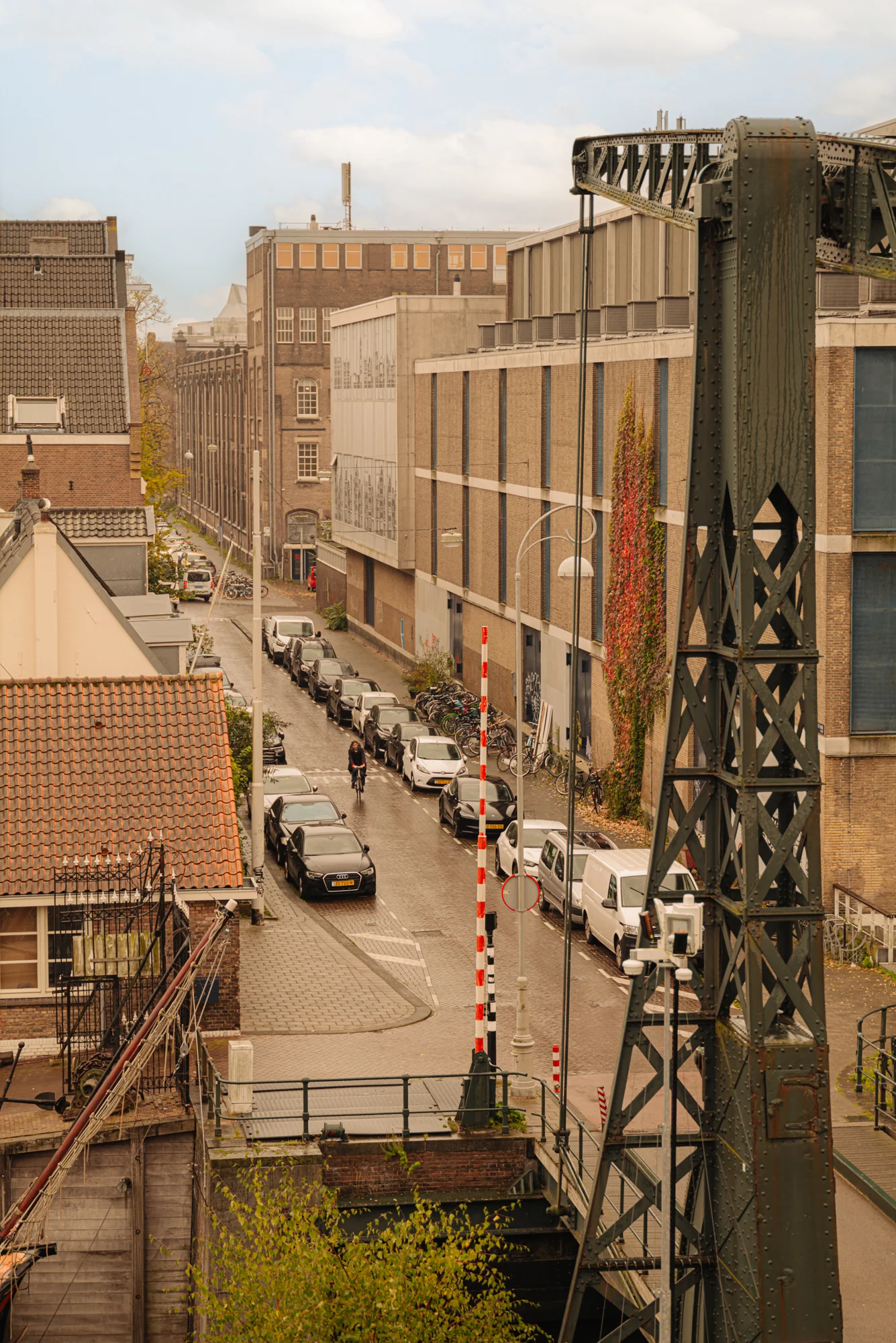 Uitzicht op de Hoogte Kadijk met auto's langs de weg en een fietser op straat in een stedelijke omgeving.