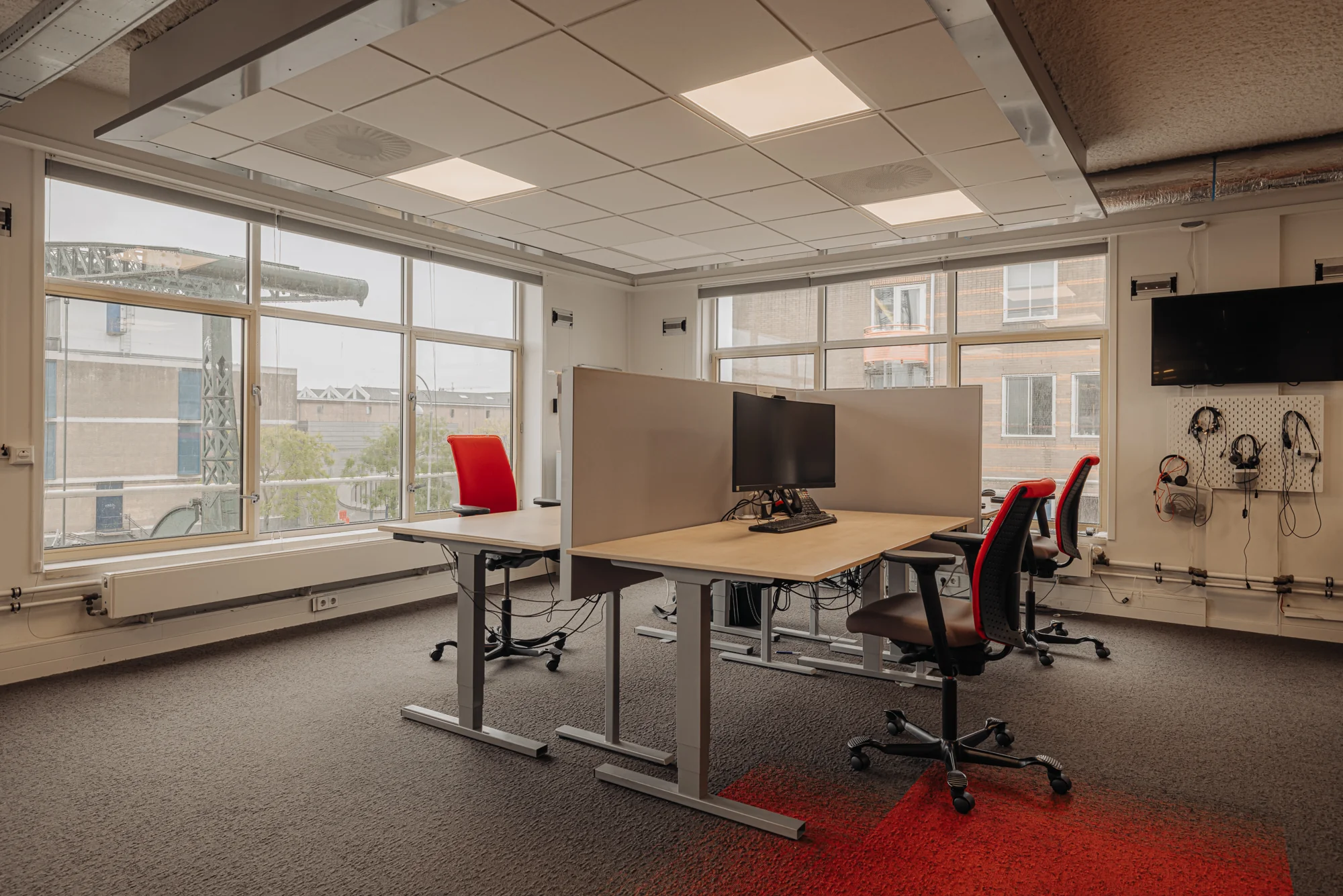 Een moderne kantoorruimte met twee bureaus, elk voorzien van een computerscherm en ergonomische stoelen, bij daglicht.