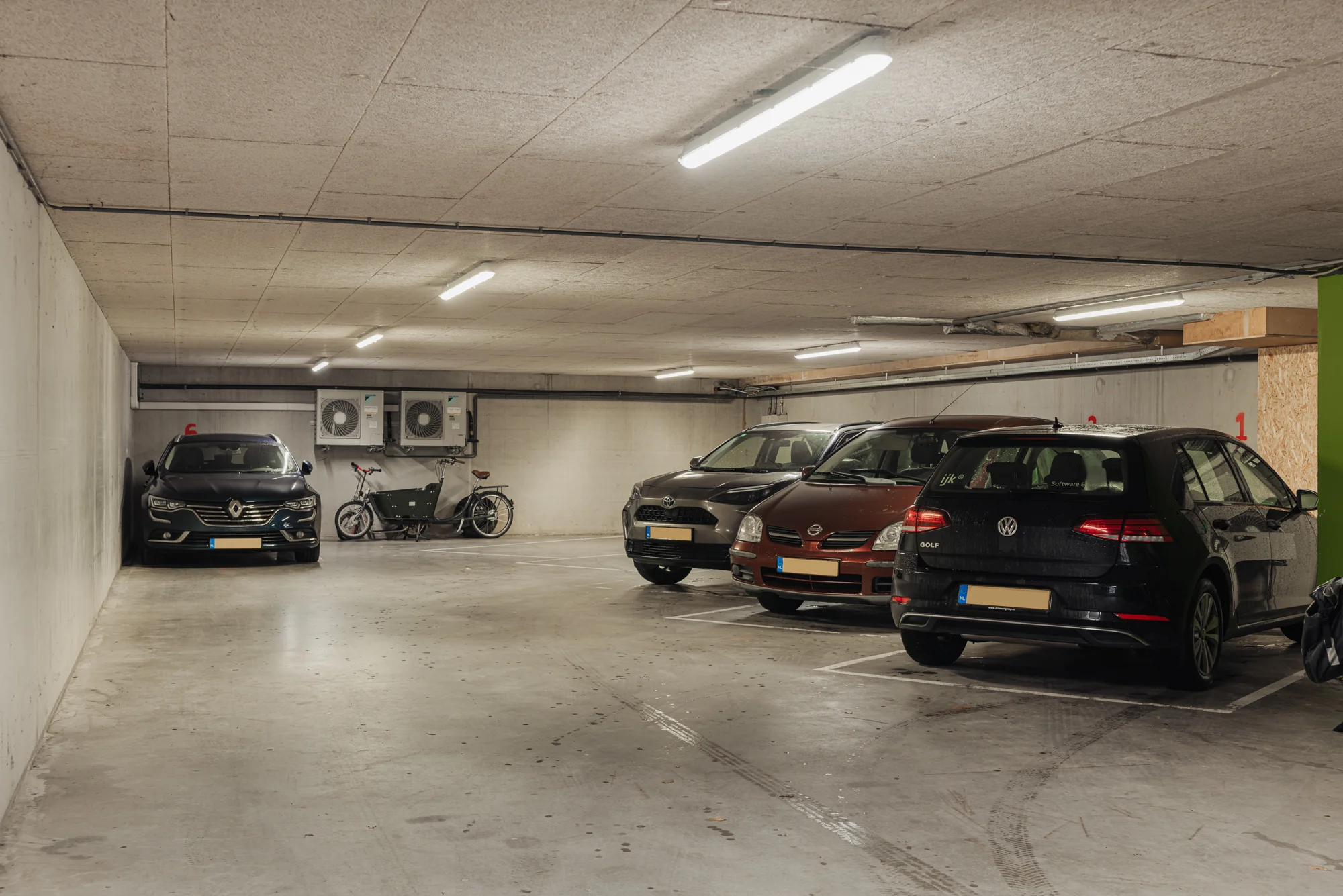 Ondergrondse parkeergarage met meerdere geparkeerde auto's en fietsen.
