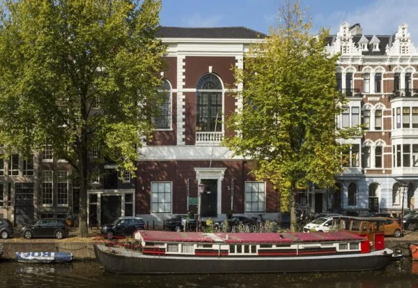 Een traditionele woonboot ligt aangemeerd aan de Keizersgracht, omringd door historische gebouwen en bomen.