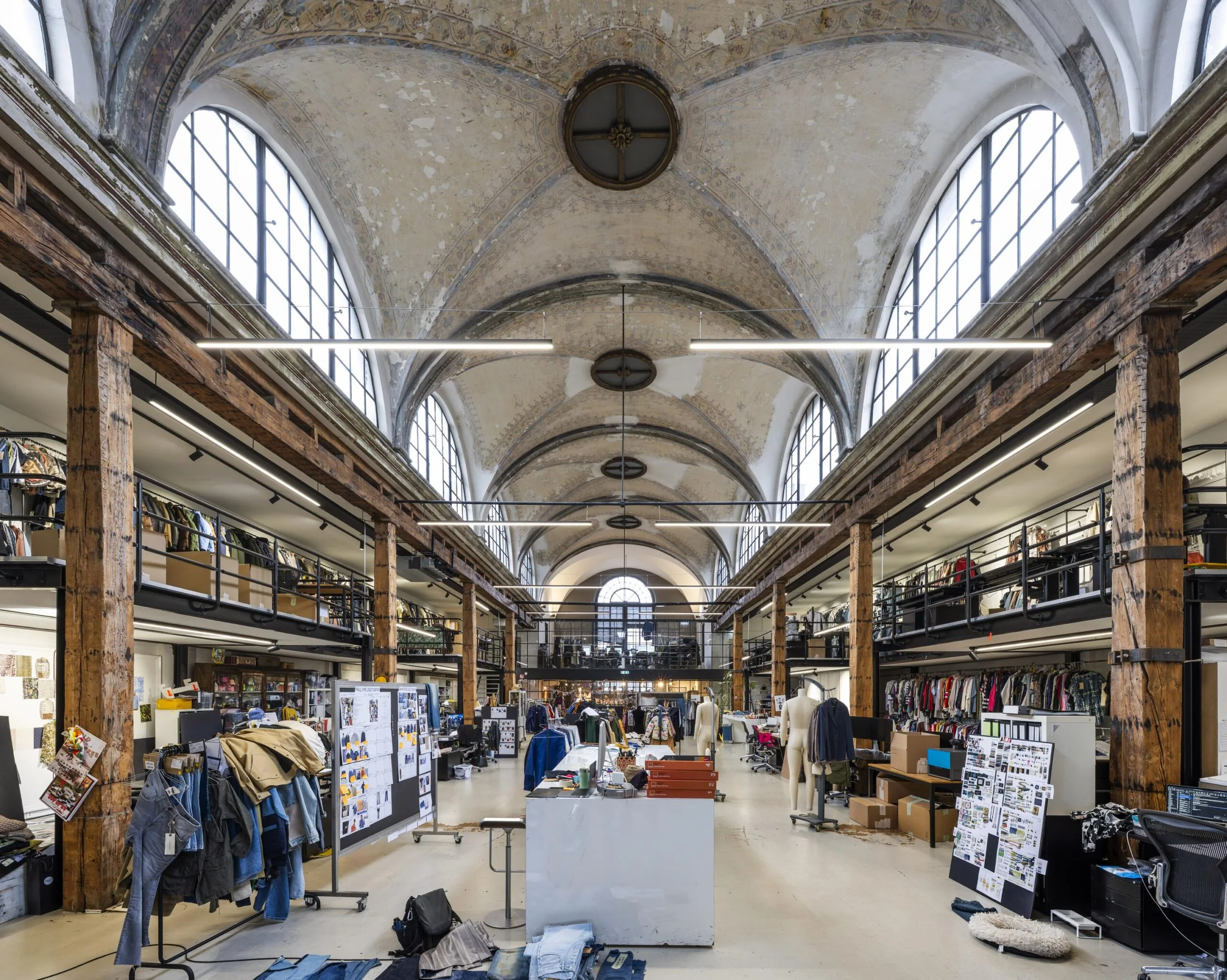 Een industriële ruimte met hoge plafonds en grote ramen aan de Keizersgracht, ingericht als creatieve werkplek met kleding en decoratie.