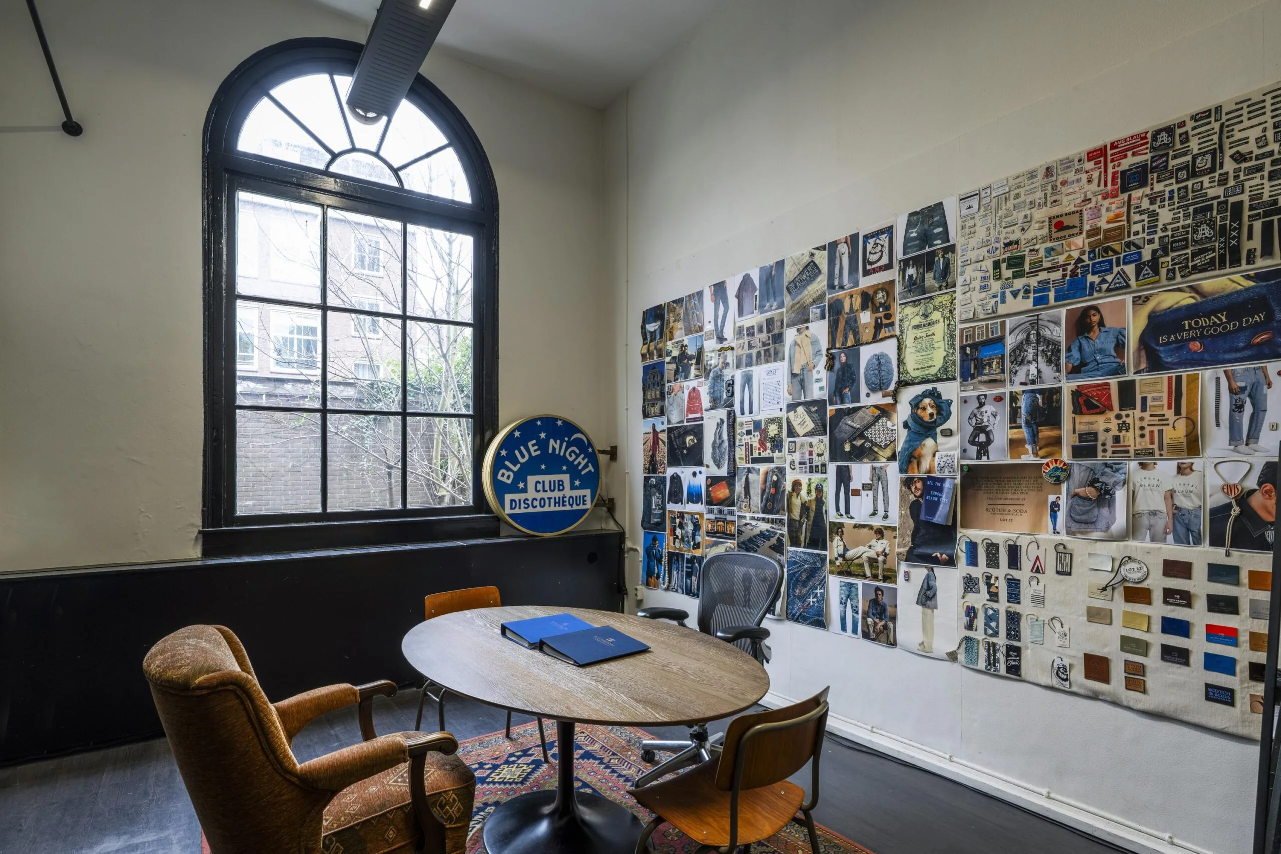 Een werkruimte aan de Keizersgracht met een ronde tafel, diverse stoelen en een muur vol foto's en afbeeldingen.