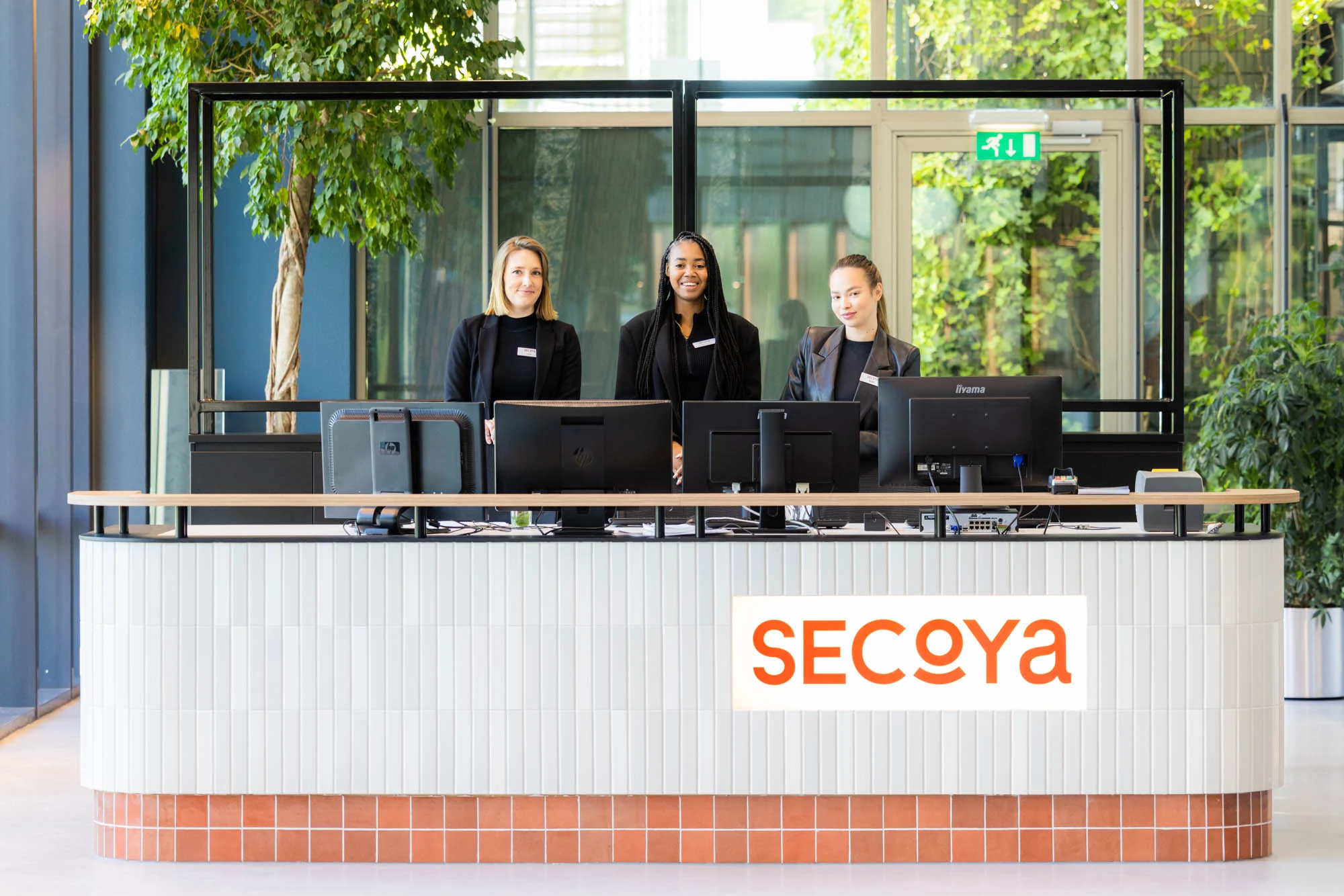 Drie medewerkers staan achter de receptiebalie van Secoya aan de Papendorpseweg.