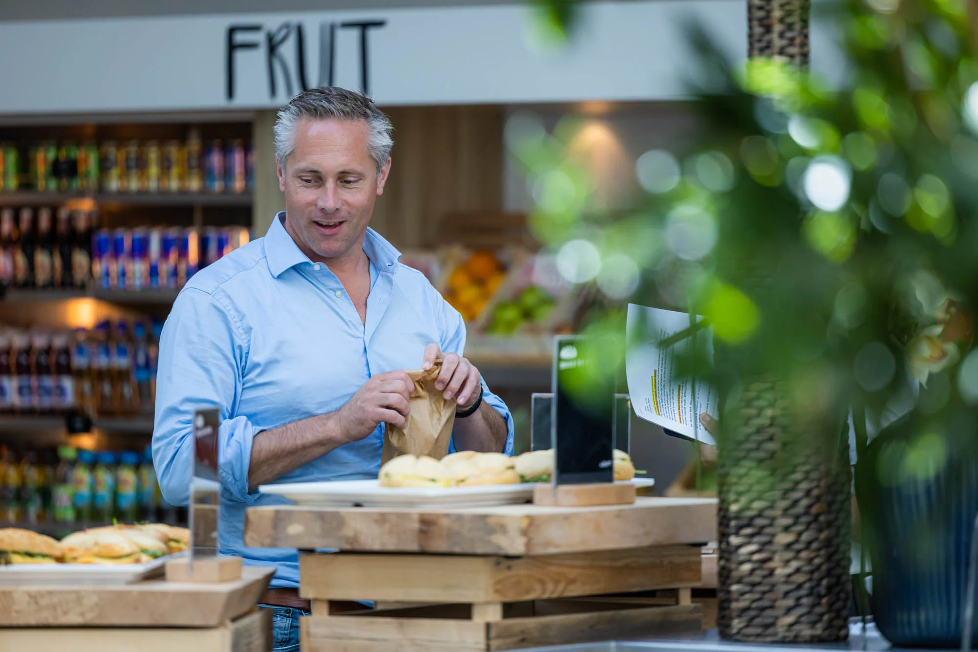 Een man in een blauwe blouse pakt een papieren zak bij een broodjeskraam naast de Papendorpseweg.