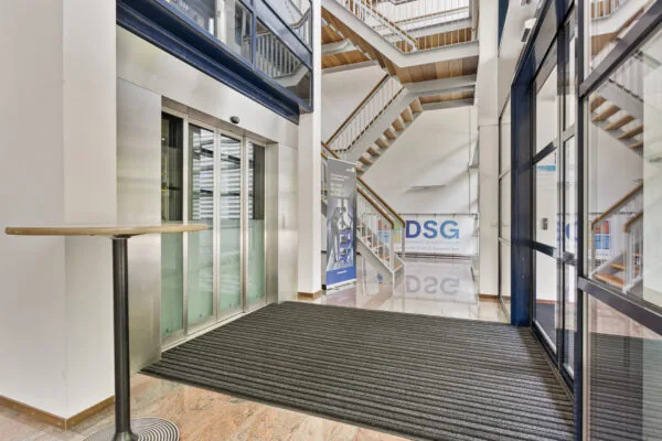 Ingang van een modern gebouw met een lift en trap, met een bord van Dynamic Service Group.