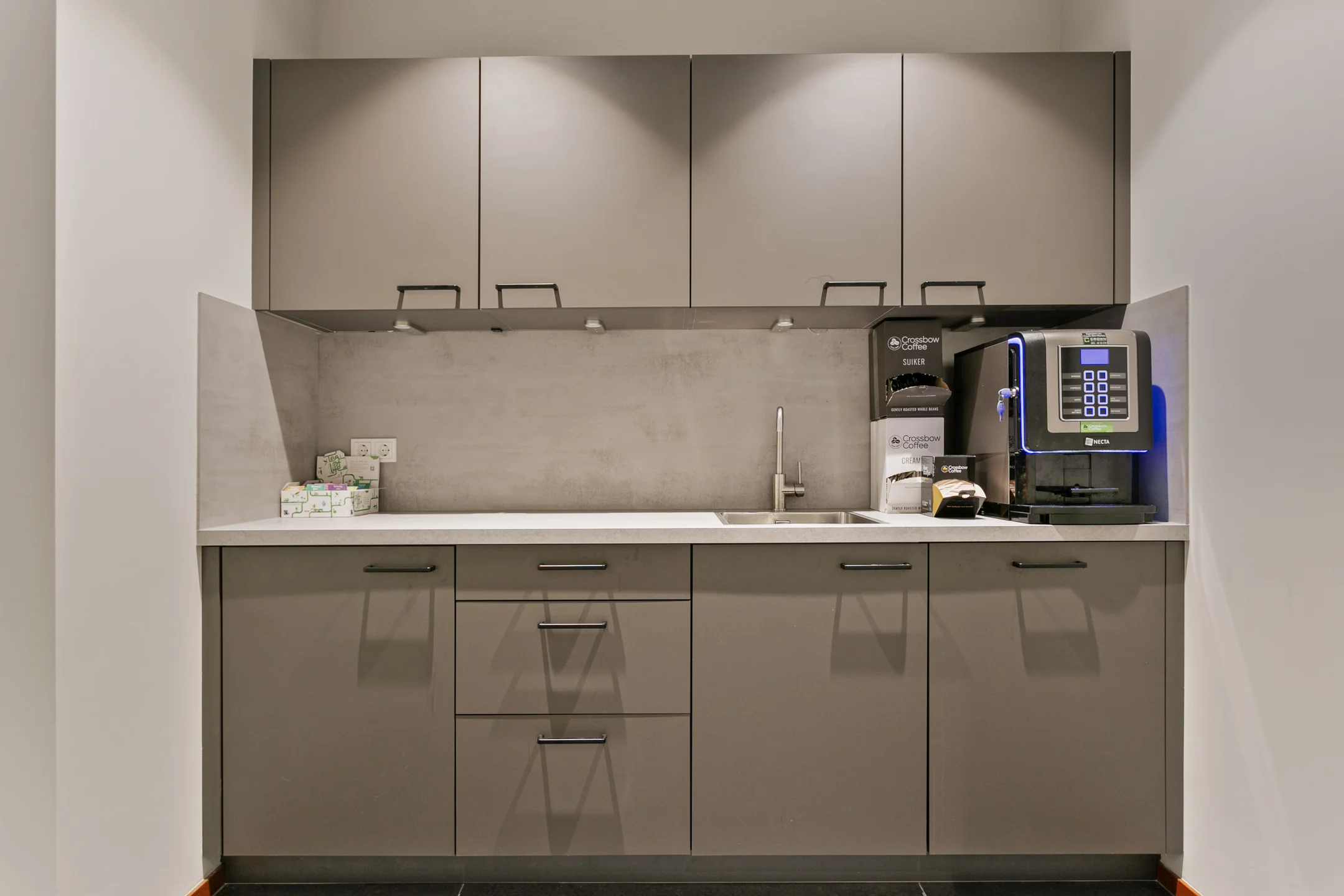 Een moderne kantoorpantry met koffiezetapparaat en spoelbak.