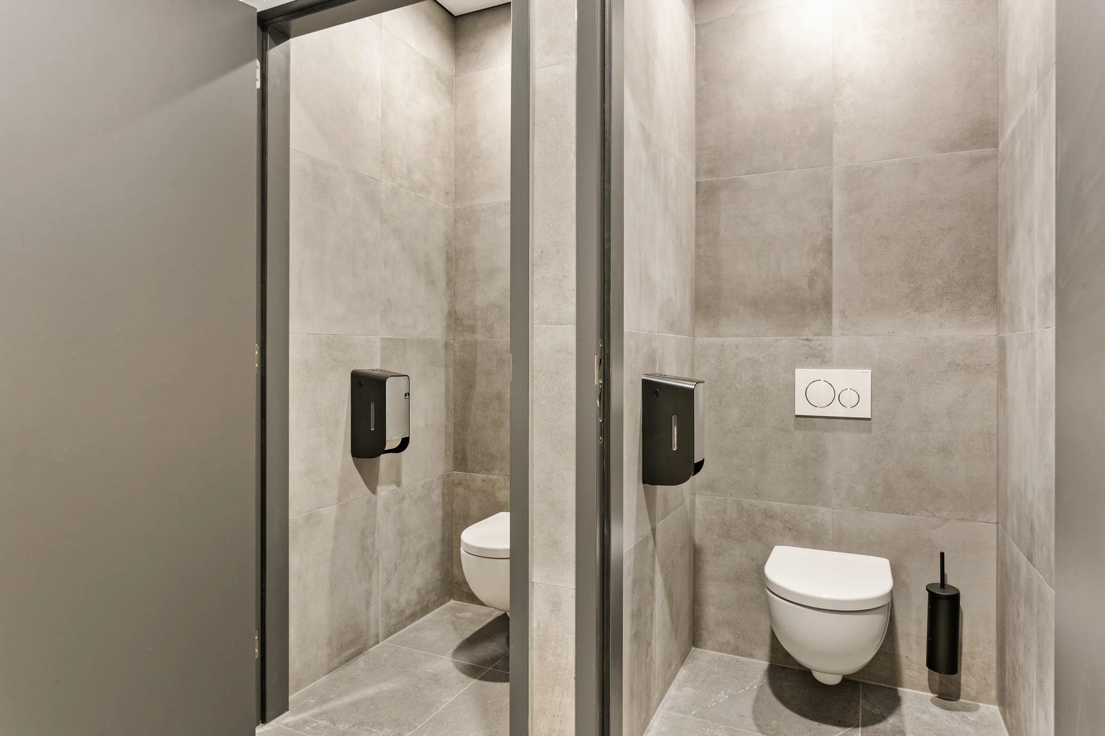 Twee moderne toiletruimtes met grijze betegeling en wandhangende toiletten.