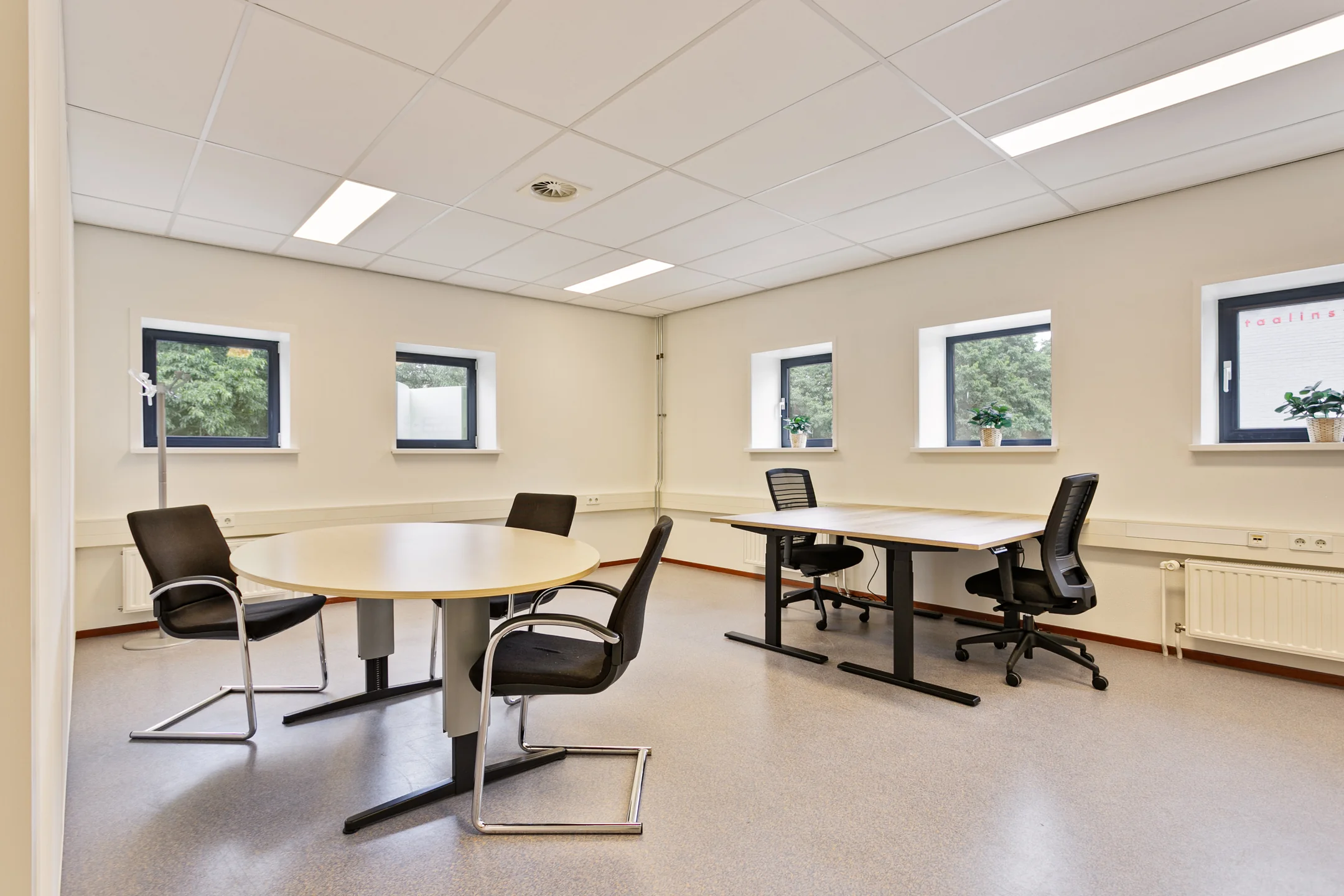 Een lichte kantoorruimte met ronde en rechthoekige tafels en meerdere bureaustoelen.