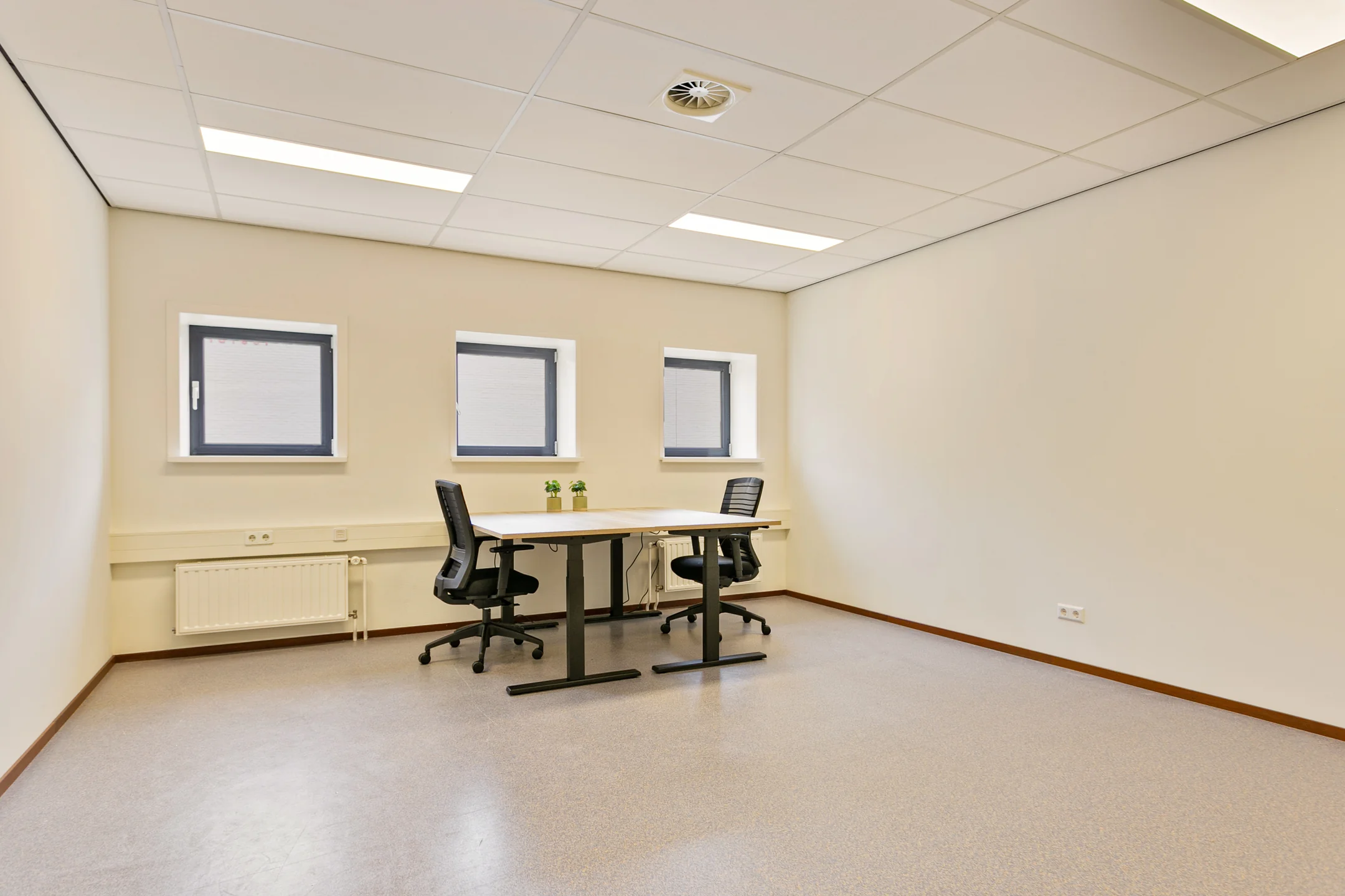 Lege kantoorruimte met twee bureaustoelen en een tafel bij een rij van drie ramen.