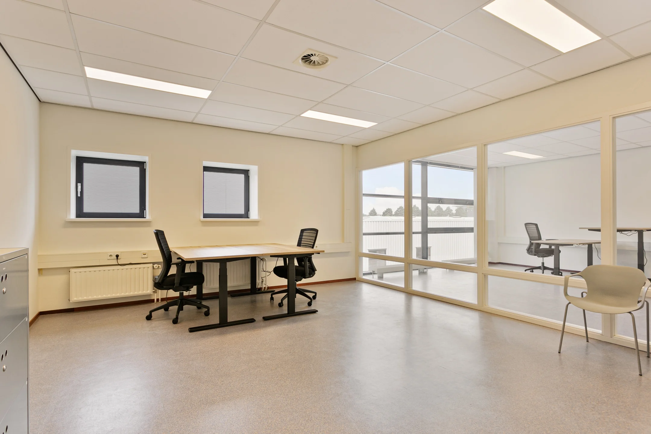 Een lege kantoorruimte met bureaus, stoelen en grote ramen.
