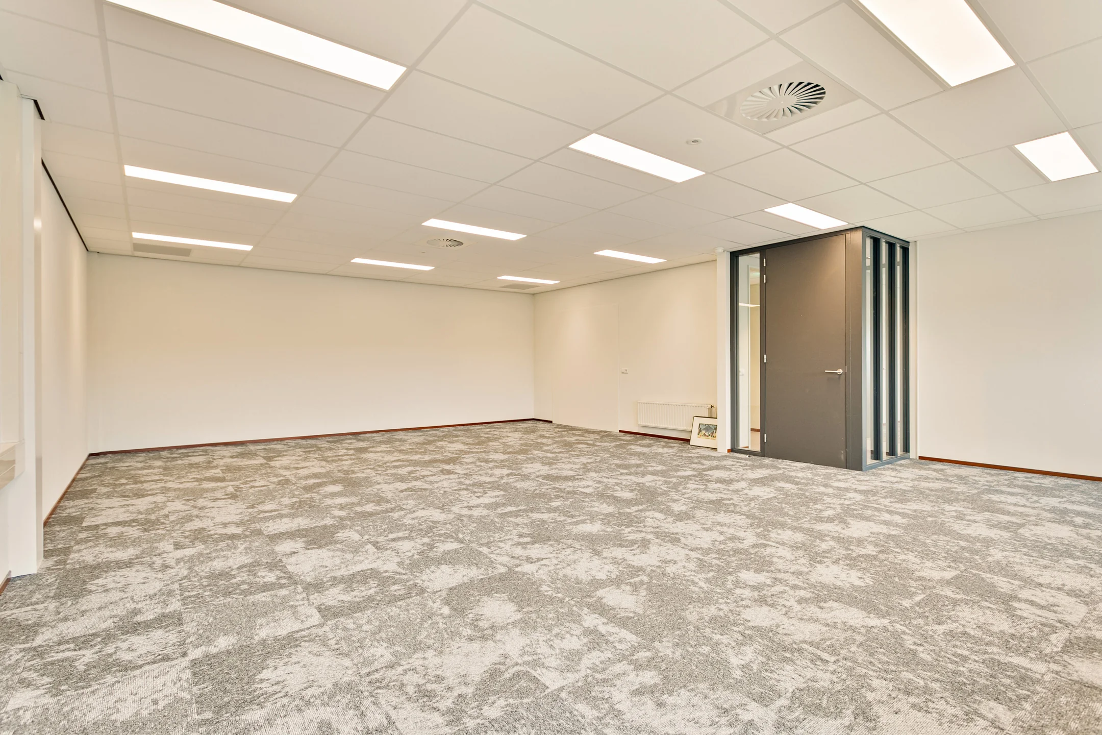Lege kamer met grijze vloerbedekking en een dichte deur.