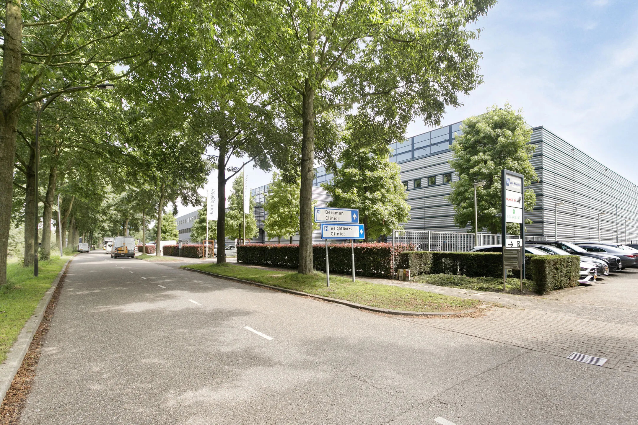 Een rustige weg met bomen leidt langs een groot, modern gebouw met parkeergelegenheid en borden voor Bergman Clinics en WeightWorks Clinics.