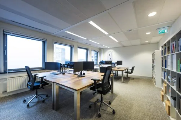 Een modern kantoorpand met houten bureaus, zwarte bureaustoelen, en grote ramen aan de Rembrandtweg.