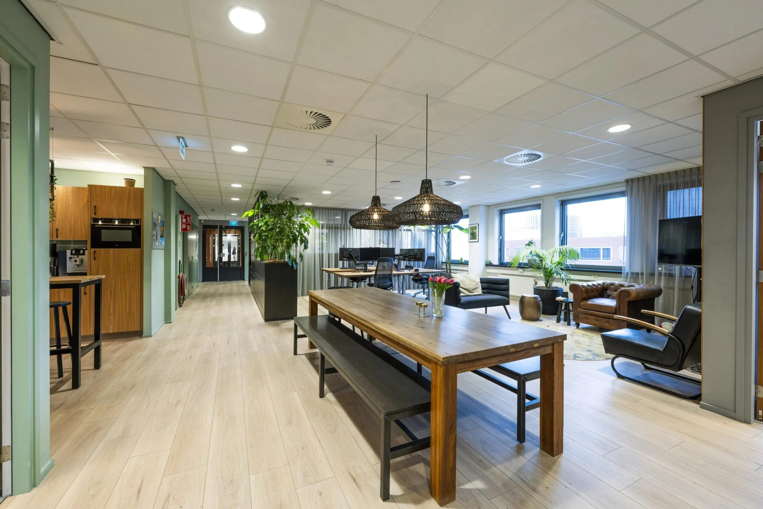 Een moderne en sfeervolle kantoorruimte met houten accenten, groene planten en comfortabele zitplekken.