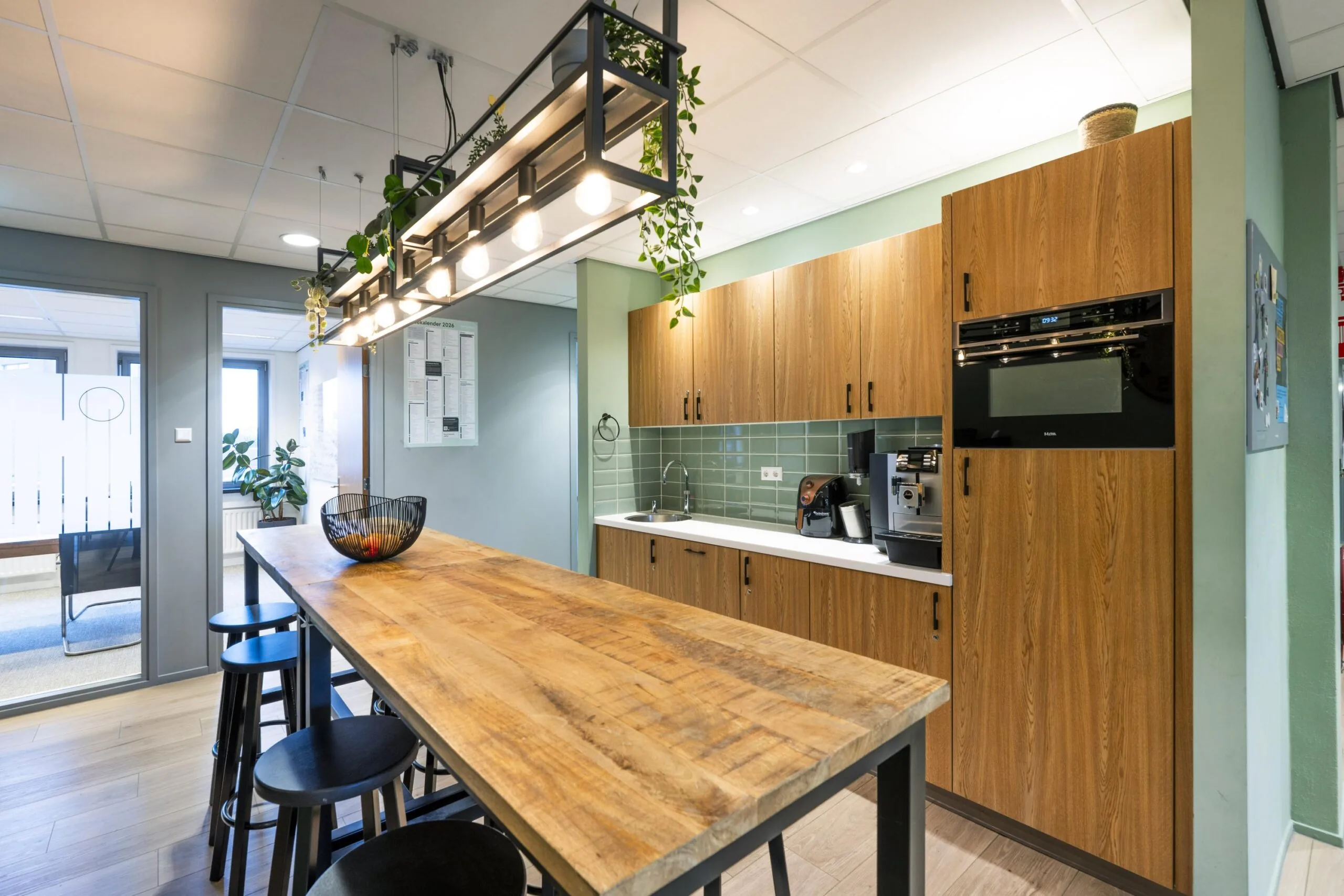 Moderne kantoor keuken met houten kasten, een lange tafel en industriële verlichting.