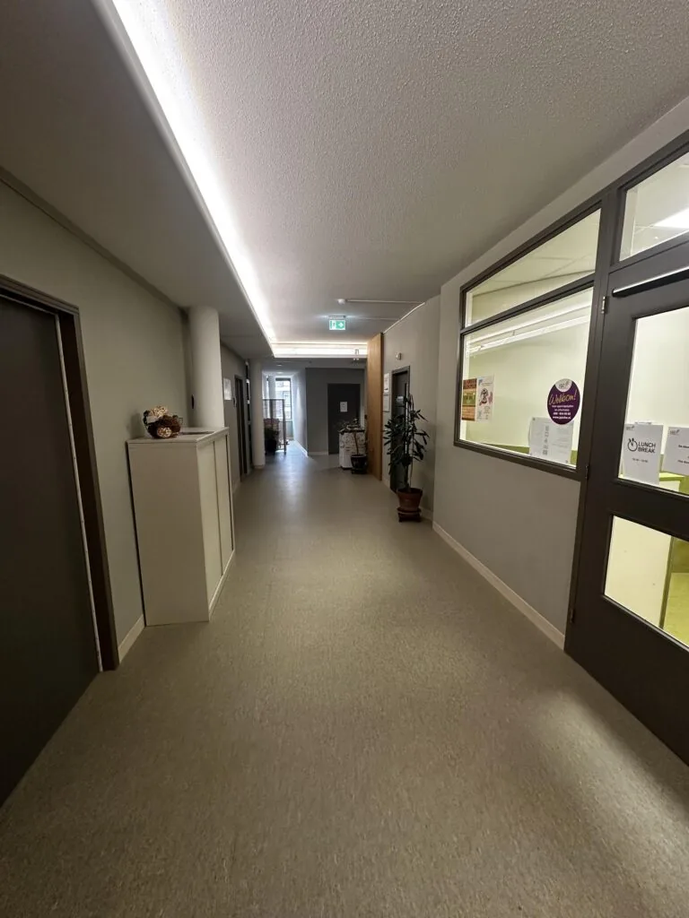 Een lange, moderne gang in een gebouw met neutrale kleuren en enkele decoratieve elementen.