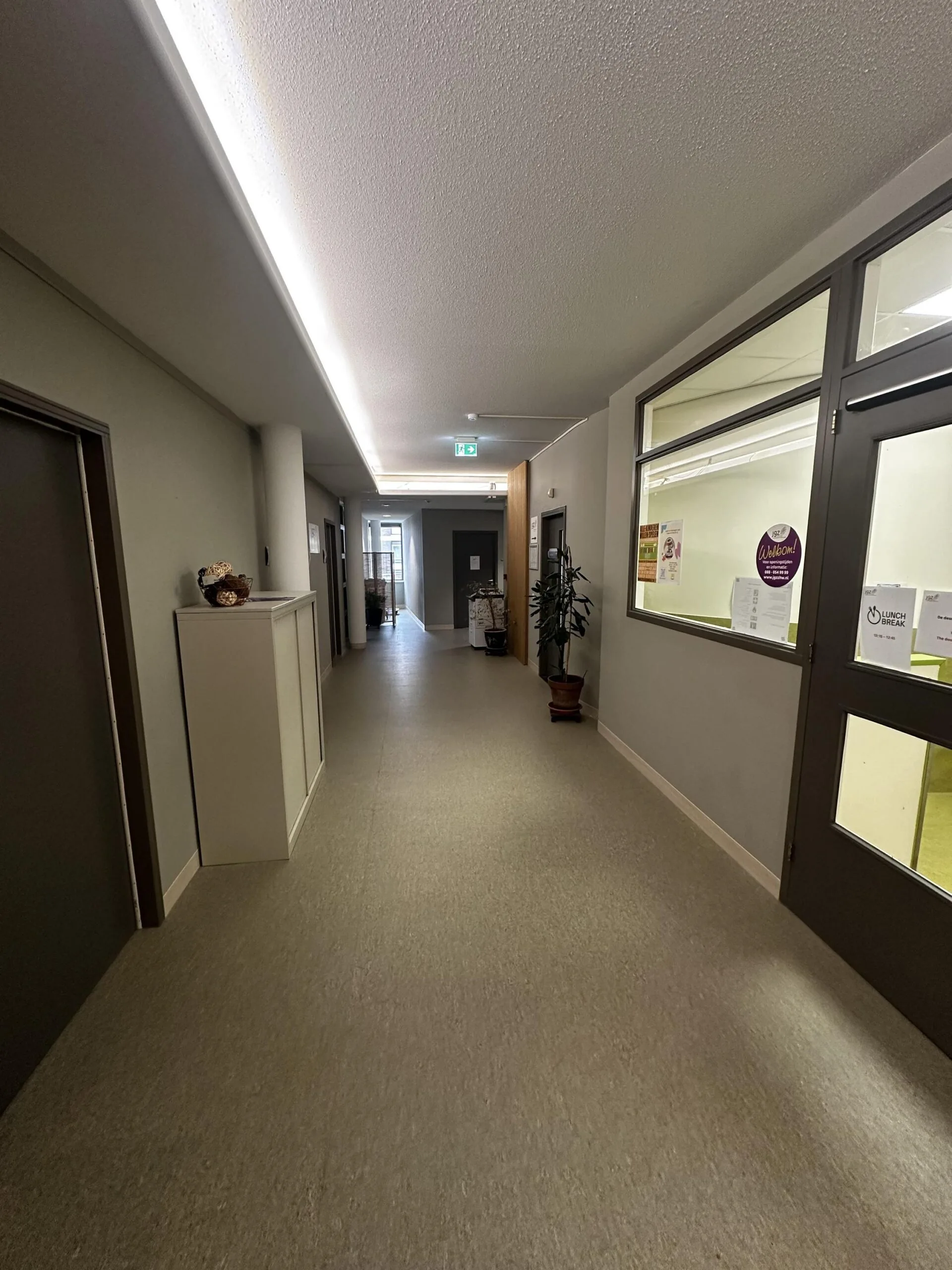 Een lange, moderne gang in een gebouw met neutrale kleuren en enkele decoratieve elementen.