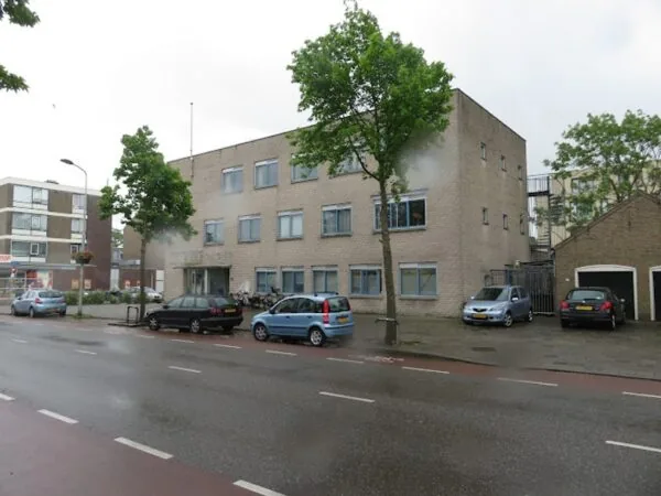 Een stenen gebouw met meerdere verdiepingen aan de Nassaulaan, met auto's geparkeerd ervoor en bomen langs de straat.