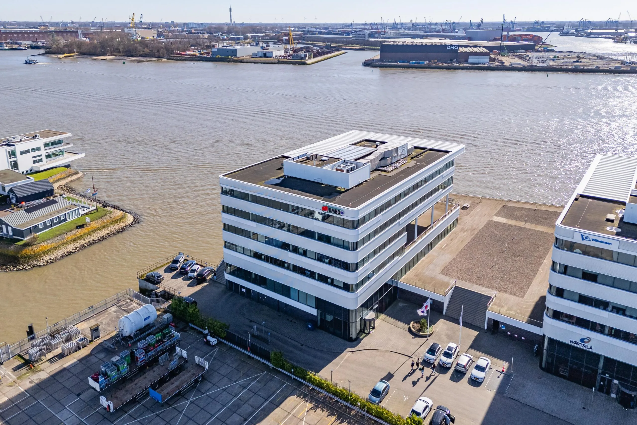 Luchtfoto van moderne kantoorgebouwen aan de Havenstraat met uitzicht op een waterweg en industriële haven in de verte.