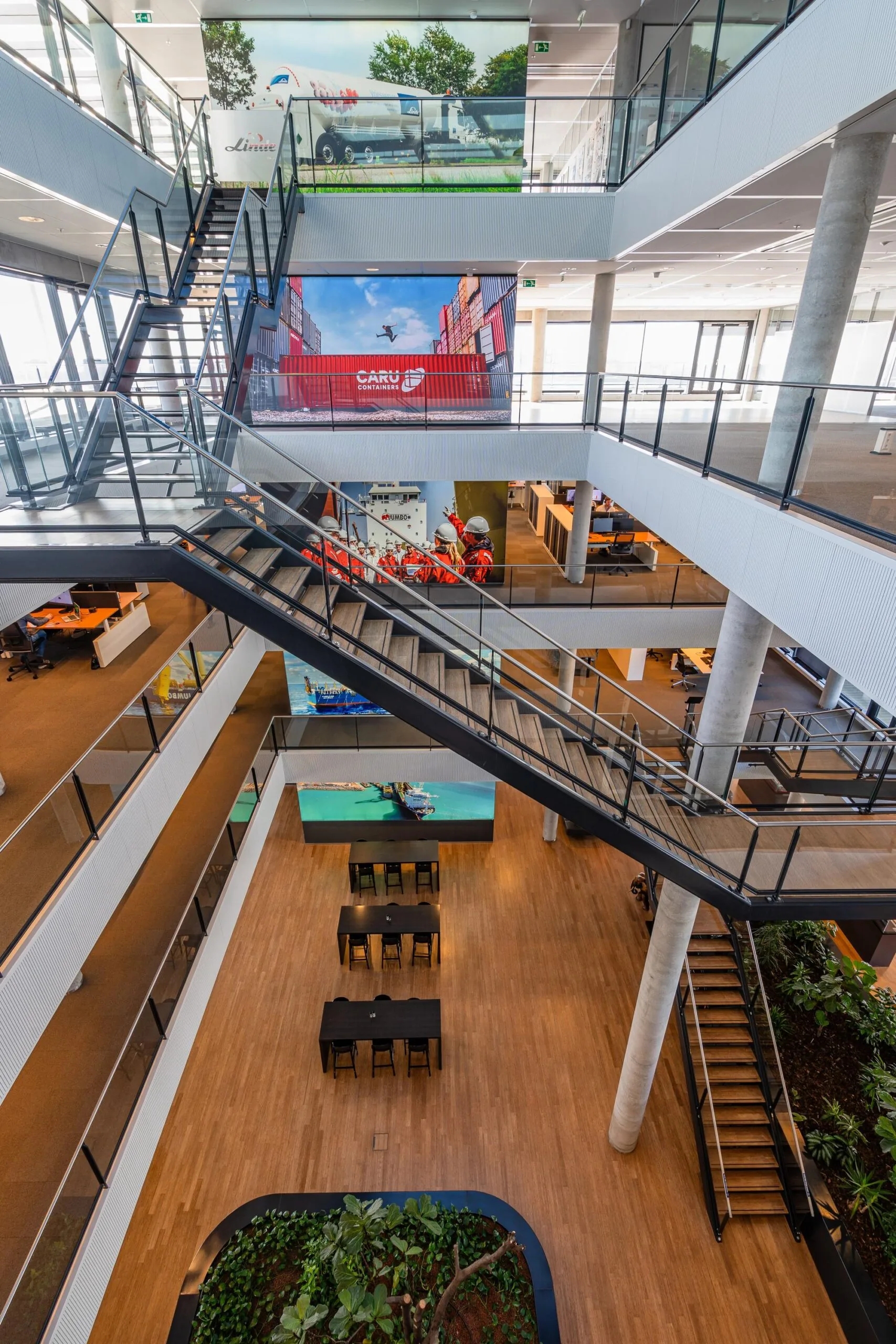 Interieur van een modern kantoor met meerdere verdiepingen, een centrale trap en wanddecoraties met transportthema's.