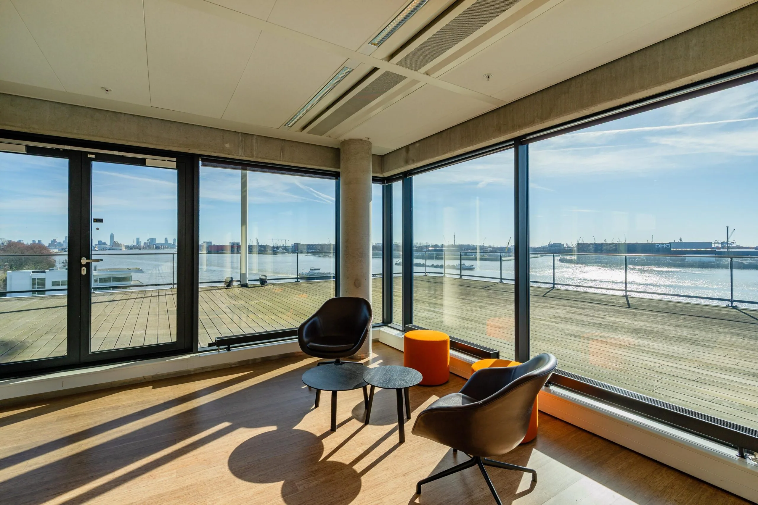Een moderne woonkamer met grote ramen biedt uitzicht op een haven onder een heldere blauwe lucht.