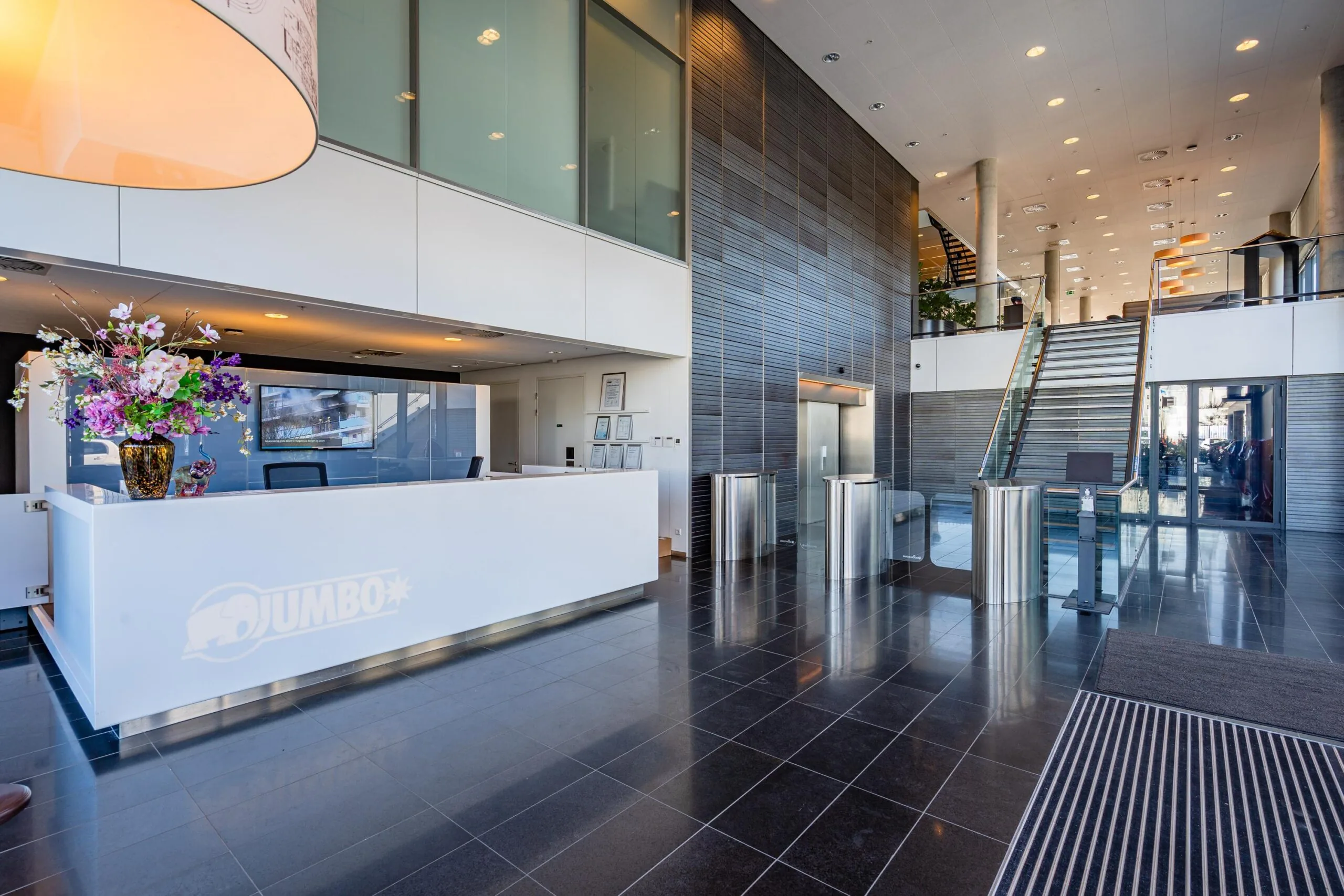 Modern kantoorinterieur met een receptiebalie en glazen trappen in een ruime lobby.