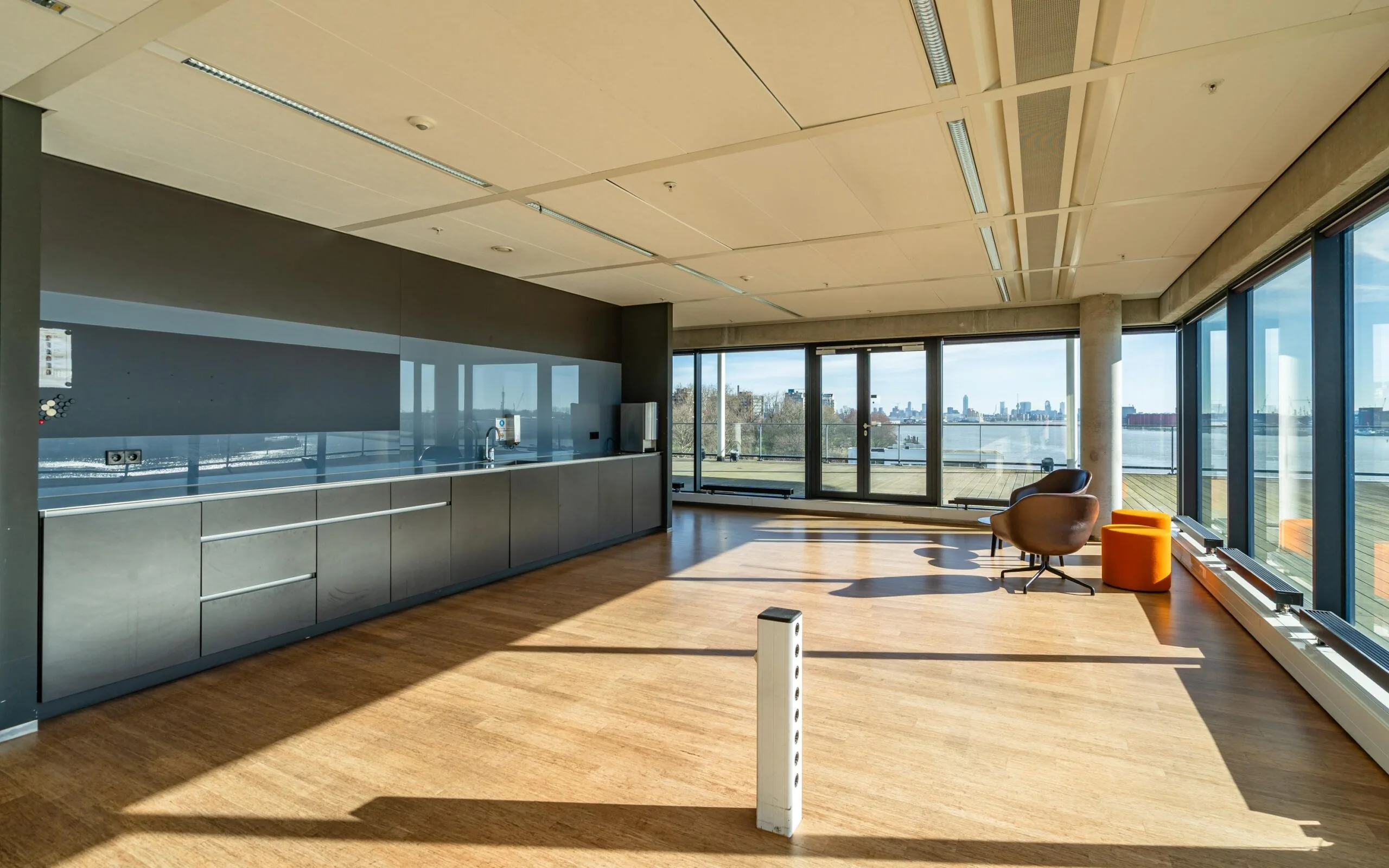 Een moderne, lichte kantoorruimte met grote ramen en uitzicht op een water en skyline.